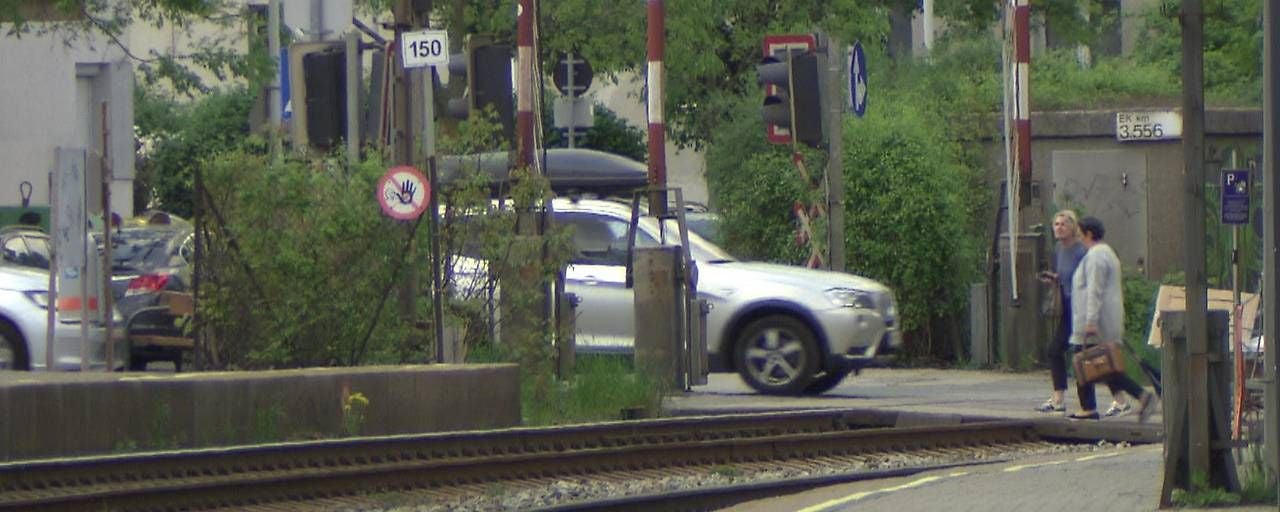 Zwei Frauen überqueren einen Bahnübergang, während ein silbernes Auto vorbeifährt.