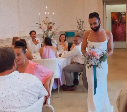 Eine Person im weißen Brautkleid hält einen Blumenstrauß und geht durch einen festlich gedeckten Saal.