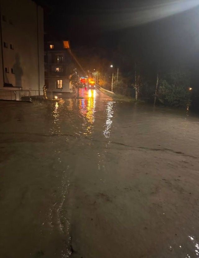 Überflutete Straße bei Nacht in Tirol mit reflektierenden Lichtern von Einsatzfahrzeugen.