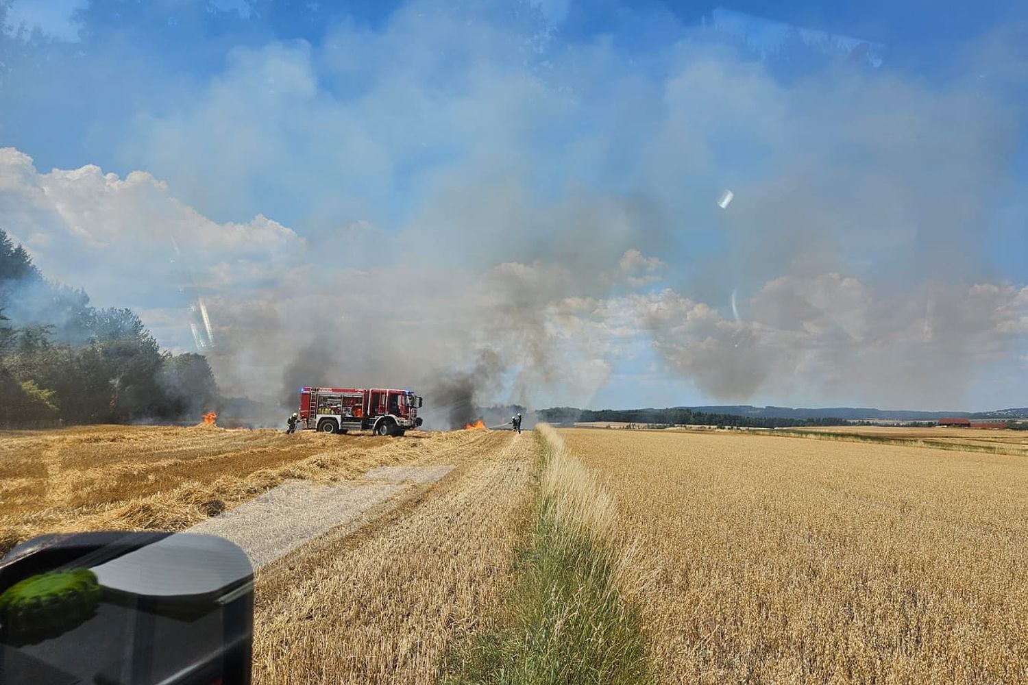 Feuerwehrauto löscht einen Feldbrand bei starkem Rauch und Hitze entlang eines Bahndamms.