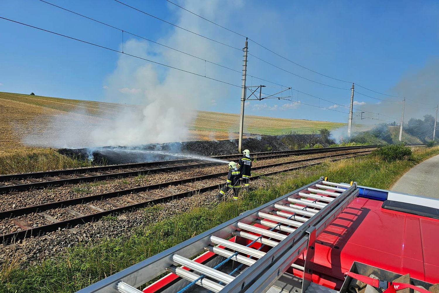 Feuerwehrleute löschen einen Böschungsbrand an Bahngleisen bei starker Rauchentwicklung.