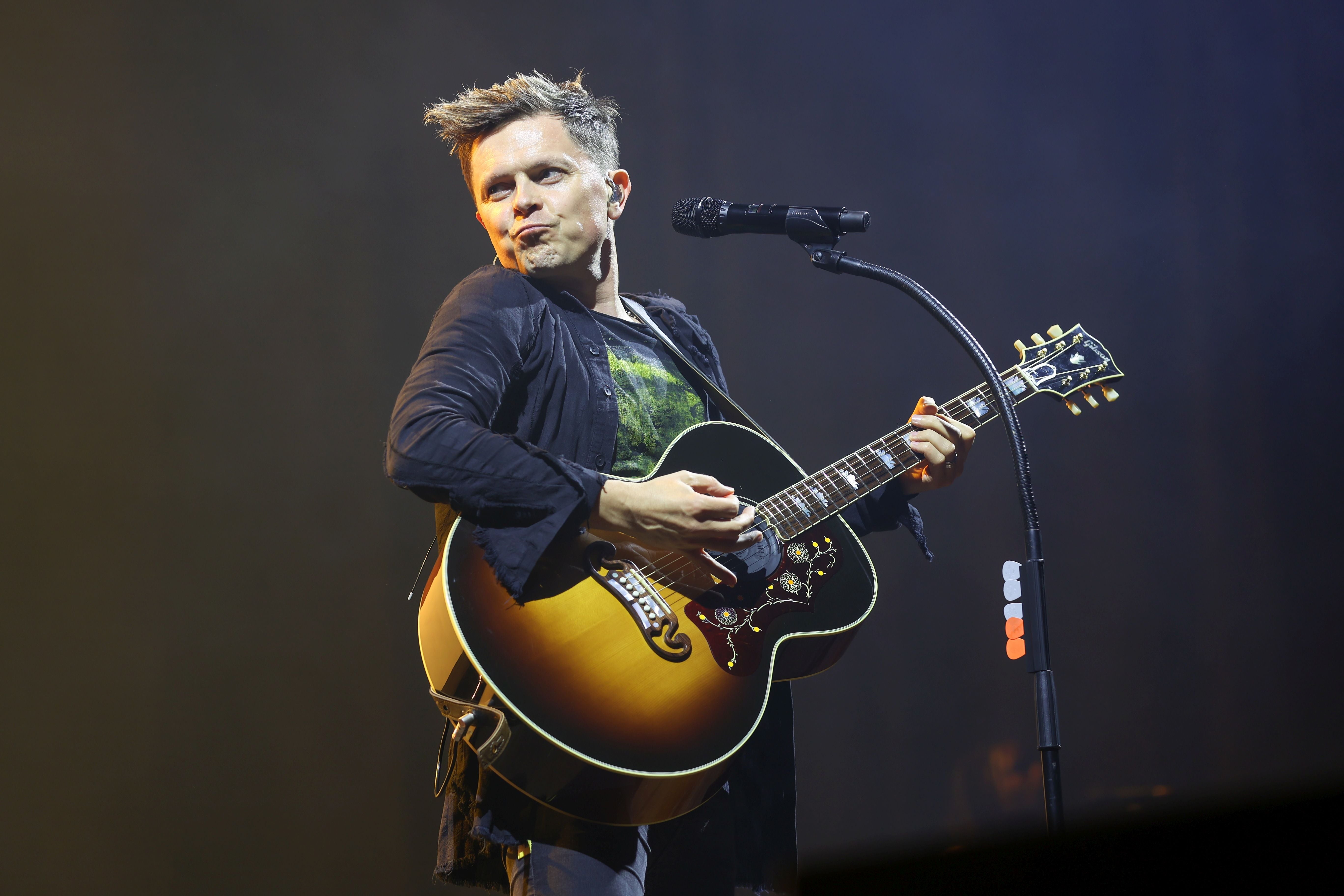 Ein Musiker spielt Gitarre und singt auf einer Bühne mit Mikrofon und Scheinwerferlicht.