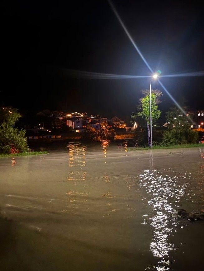 Nächtliche Überschwemmung in Tirol, Wasser bedeckt Straßen, beleuchtete Häuser im Hintergrund.