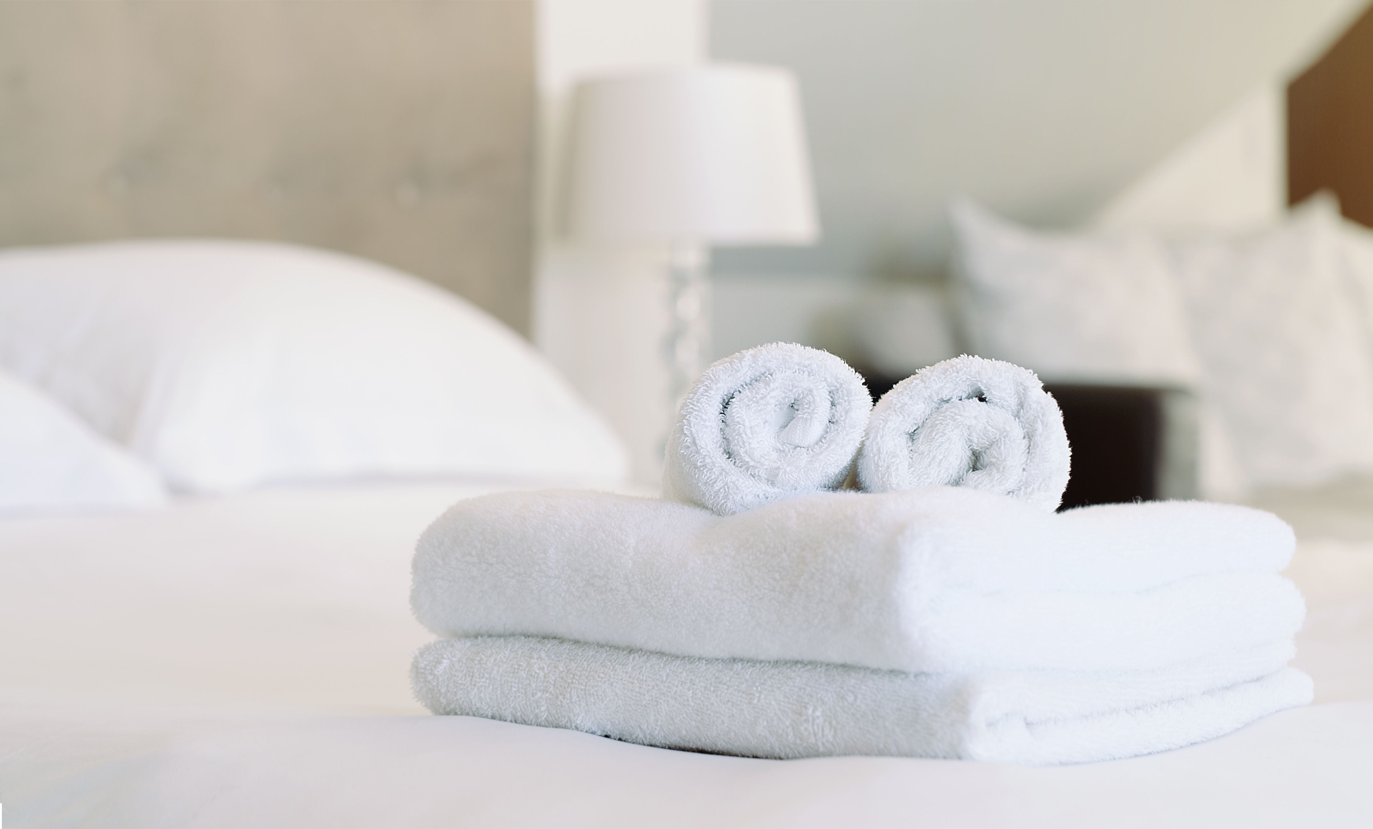 Zwei gefaltete und zwei gerollte weiße Handtücher liegen auf einem frisch gemachten Bett.