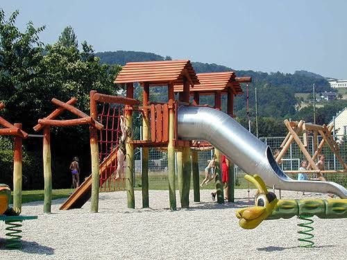 Ein moderner Spielplatz mit Rutsche, Klettergerüst und Wippe im Freien bei sonnigem Wetter.