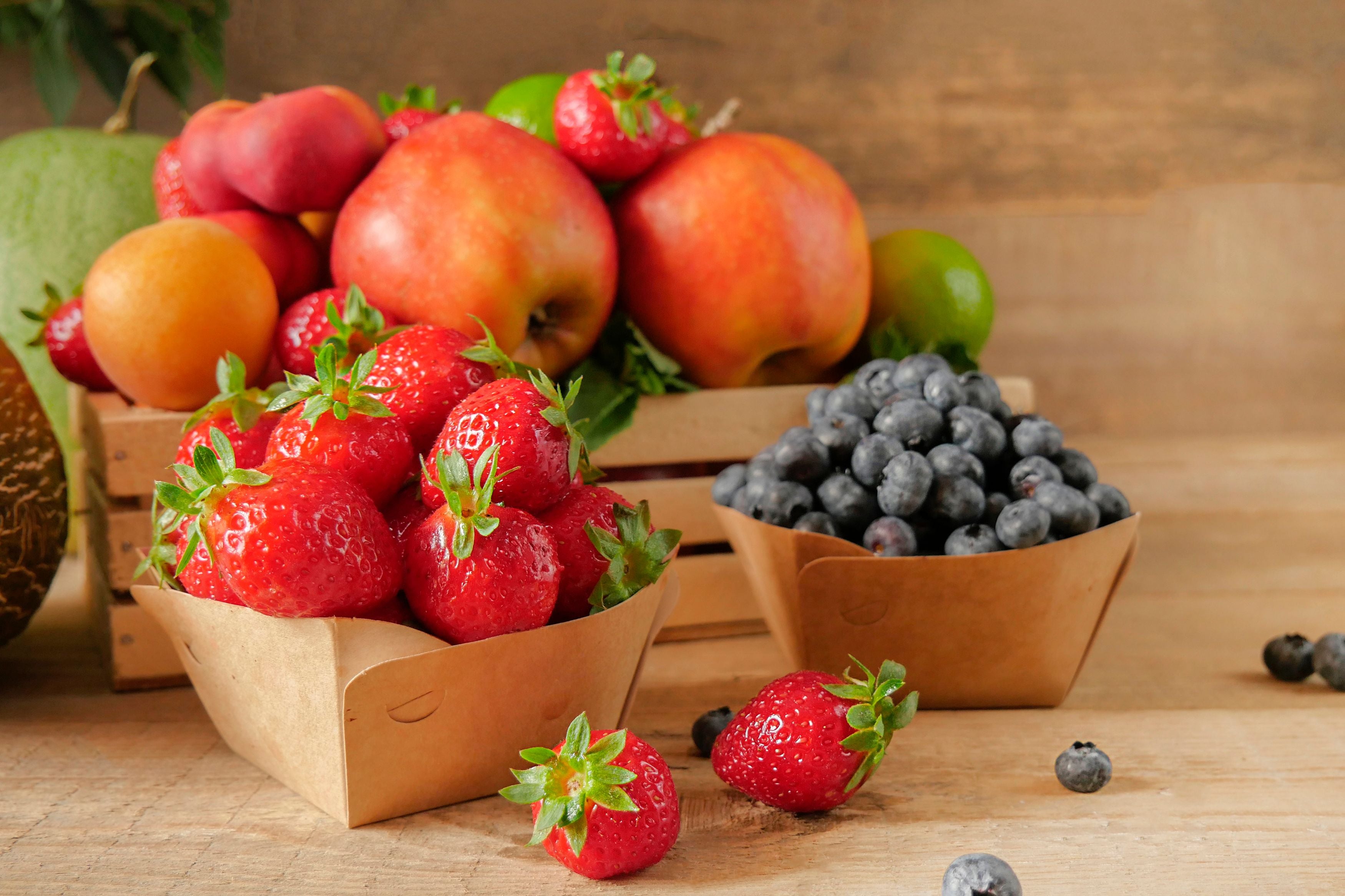 Frisches Obst, darunter Erdbeeren, Blaubeeren, Äpfel, Pfirsiche und Aprikosen auf Holztisch.