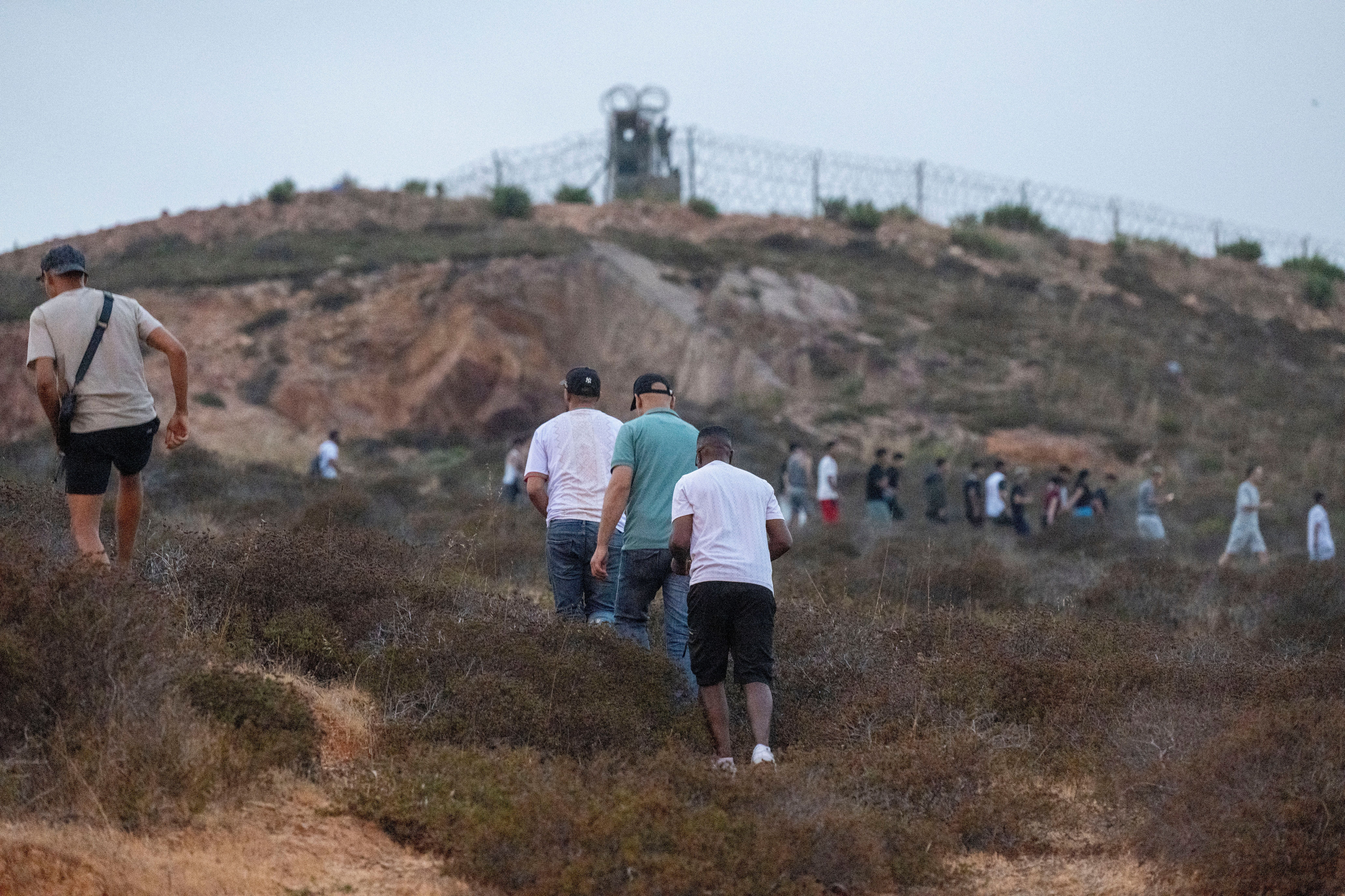Menschen gehen über eine Hügel-Landschaft in Richtung eines Grenzzauns bei Ceuta in Marokko.