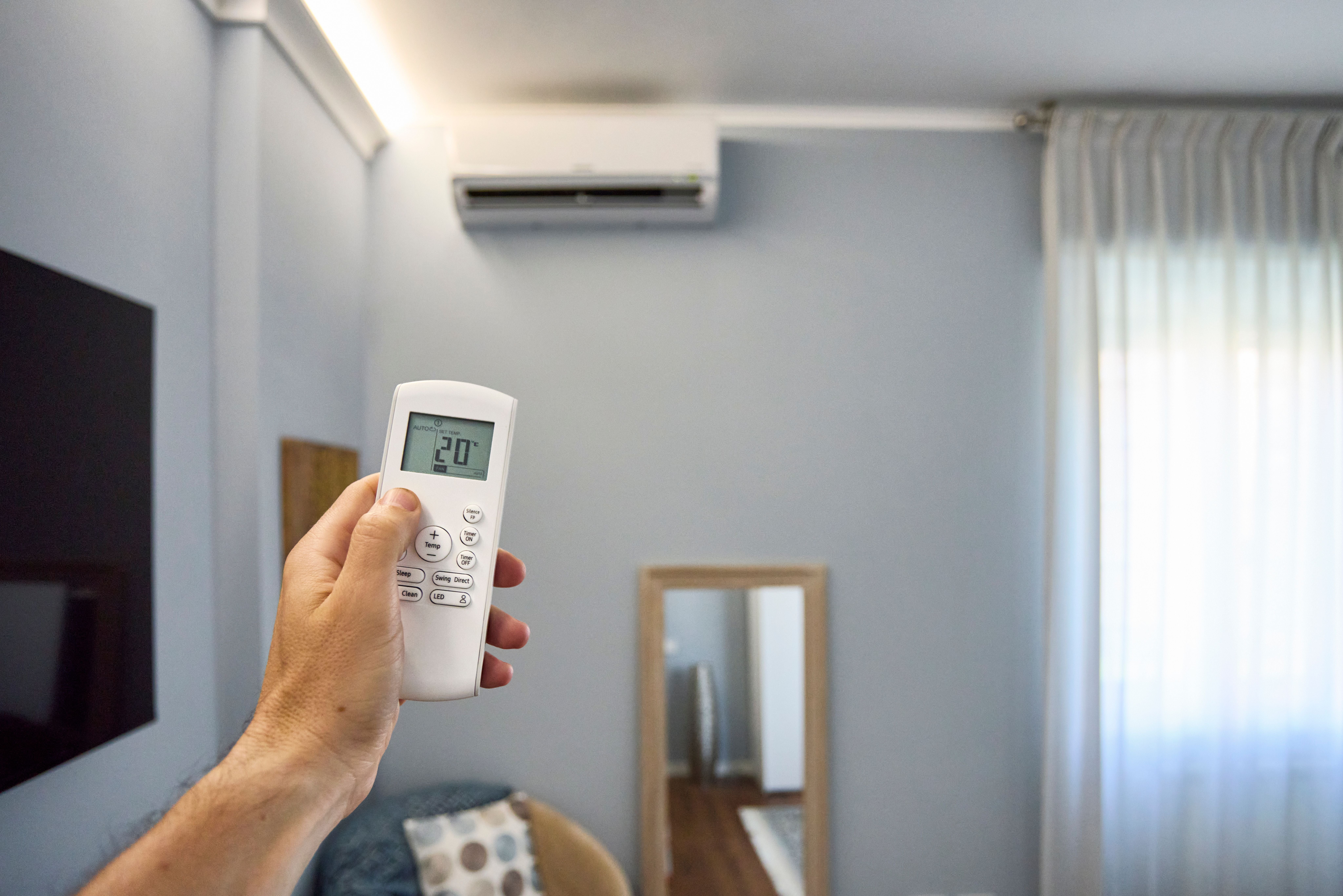 Hand hält eine Fernbedienung und richtet sie auf eine Klimaanlage im modernen Wohnzimmer.