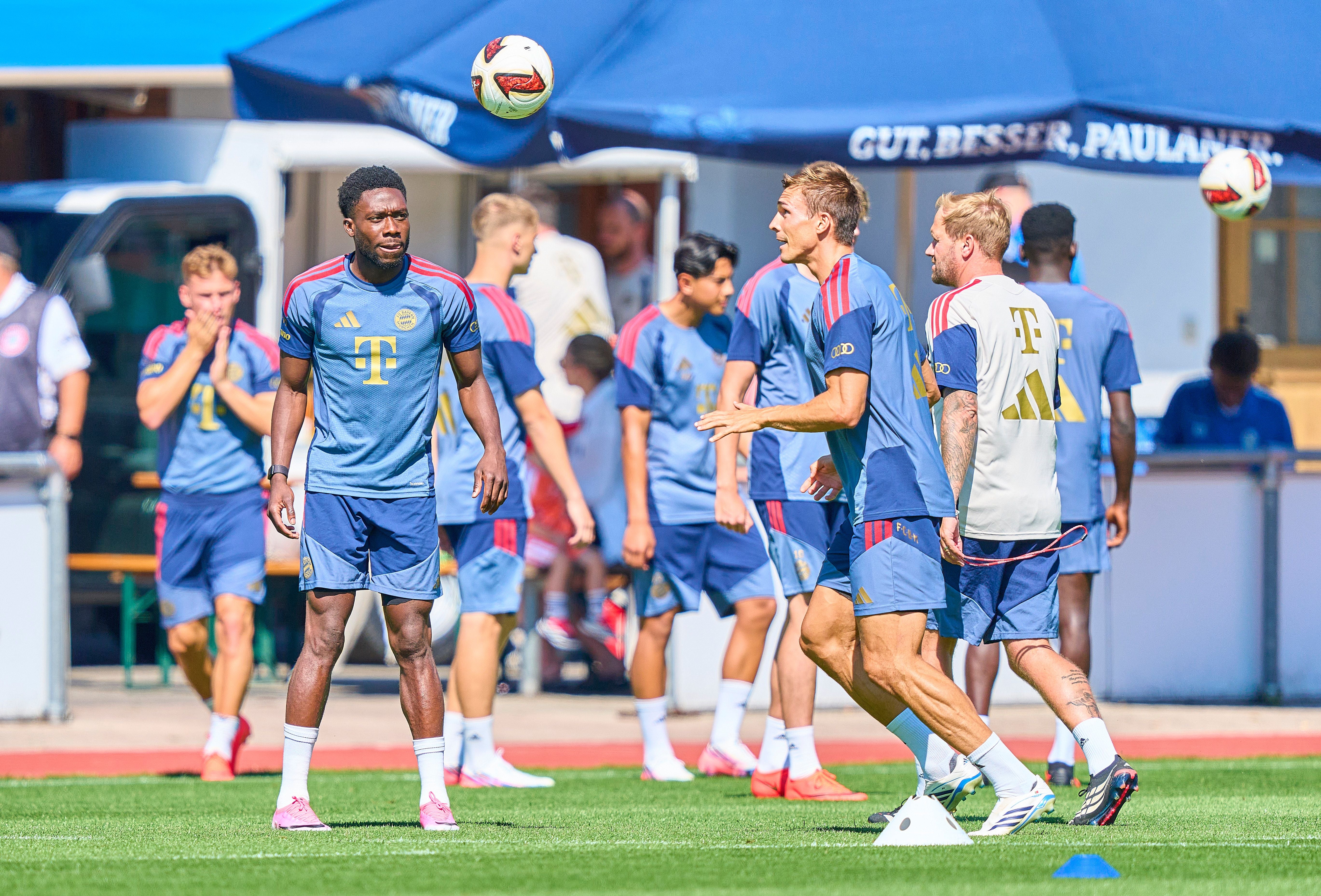 Mehrere Fußballspieler vom FC Bayern beim Training auf einem Rasenplatz bei Sonnenschein.
