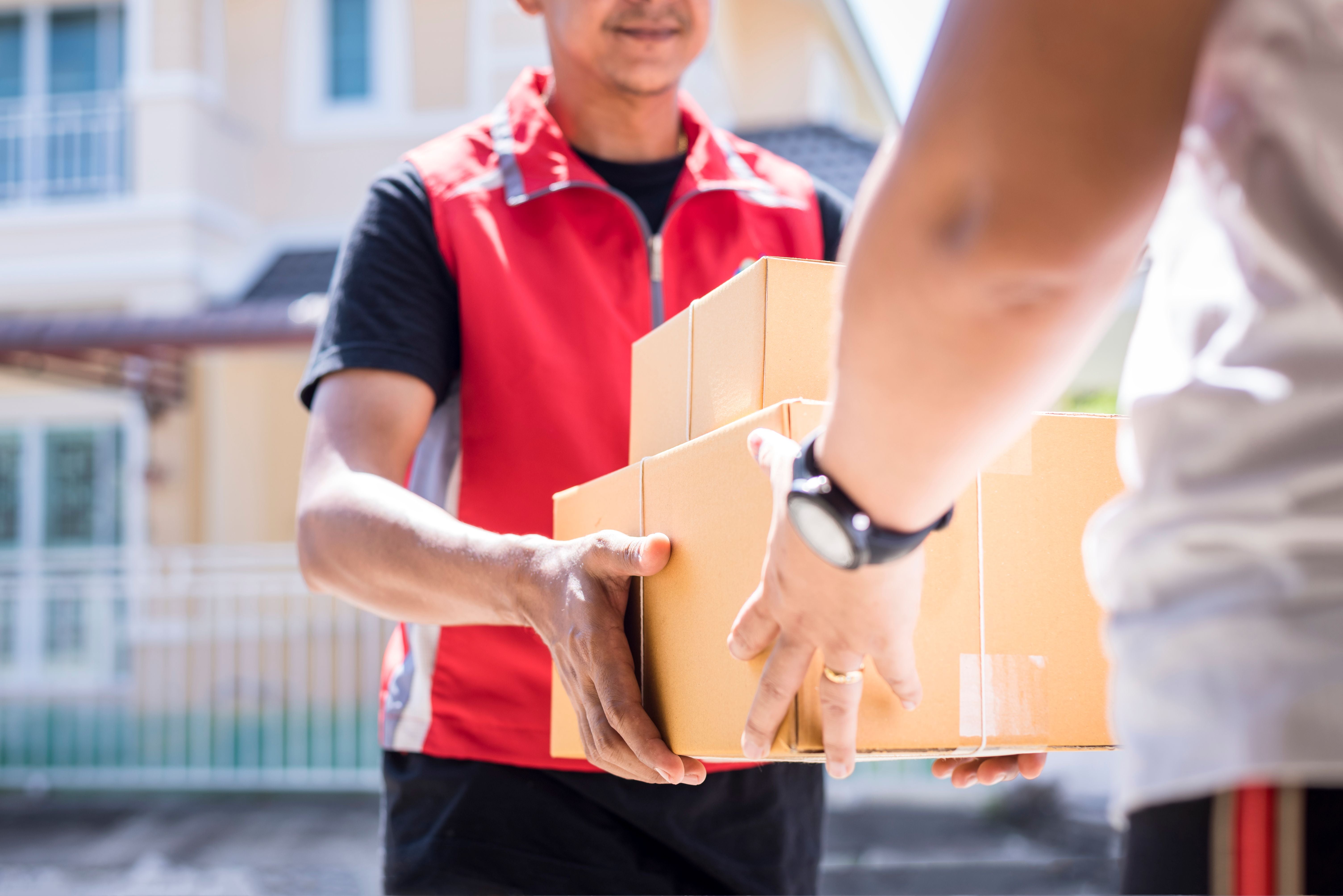 Ein Paketbote übergibt mehrere Kartons an einen Kunden vor einem Haus.