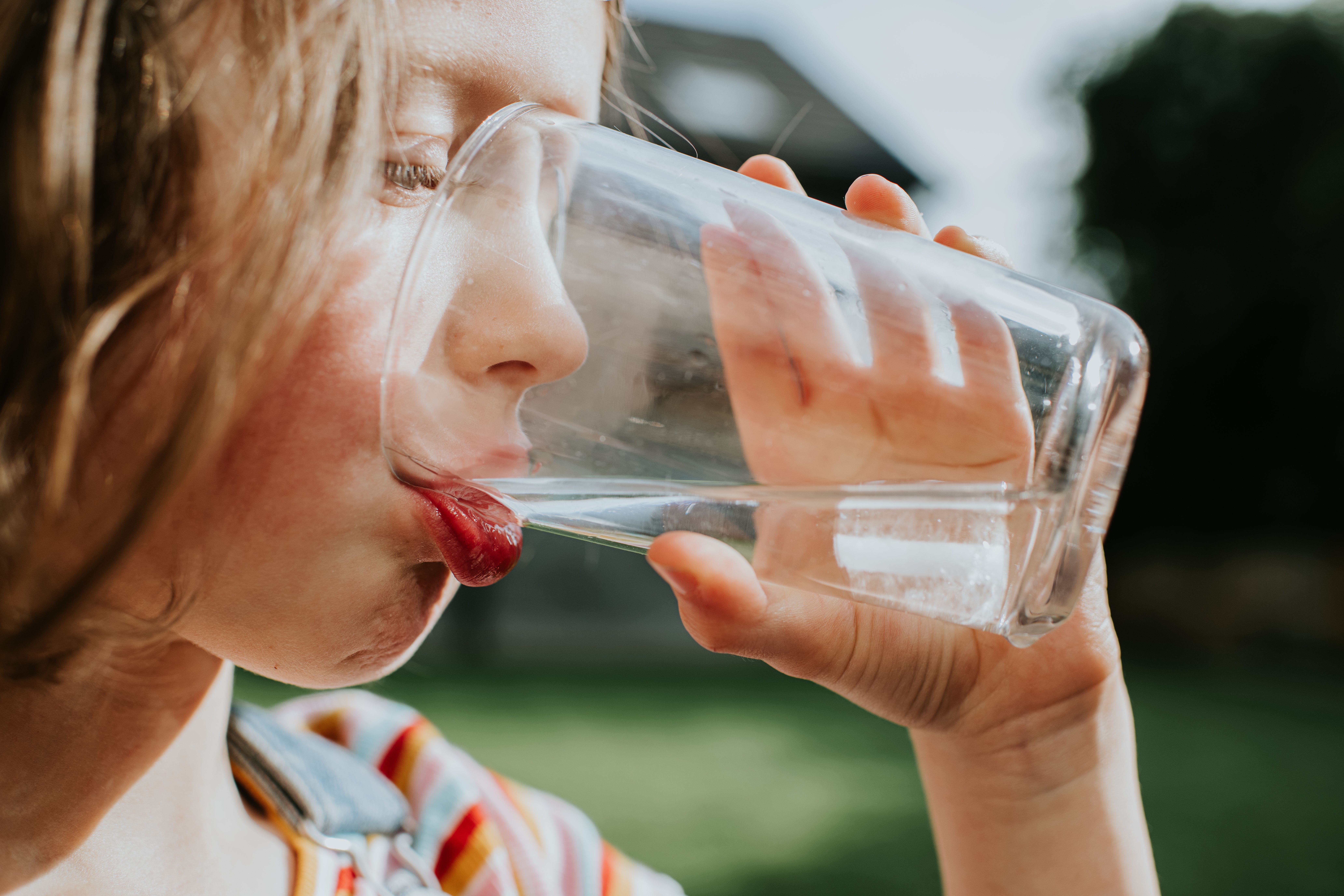 Mädchen trinkt an einem sonnigen Tag Wasser mit Eis aus einem Glas im Garten.