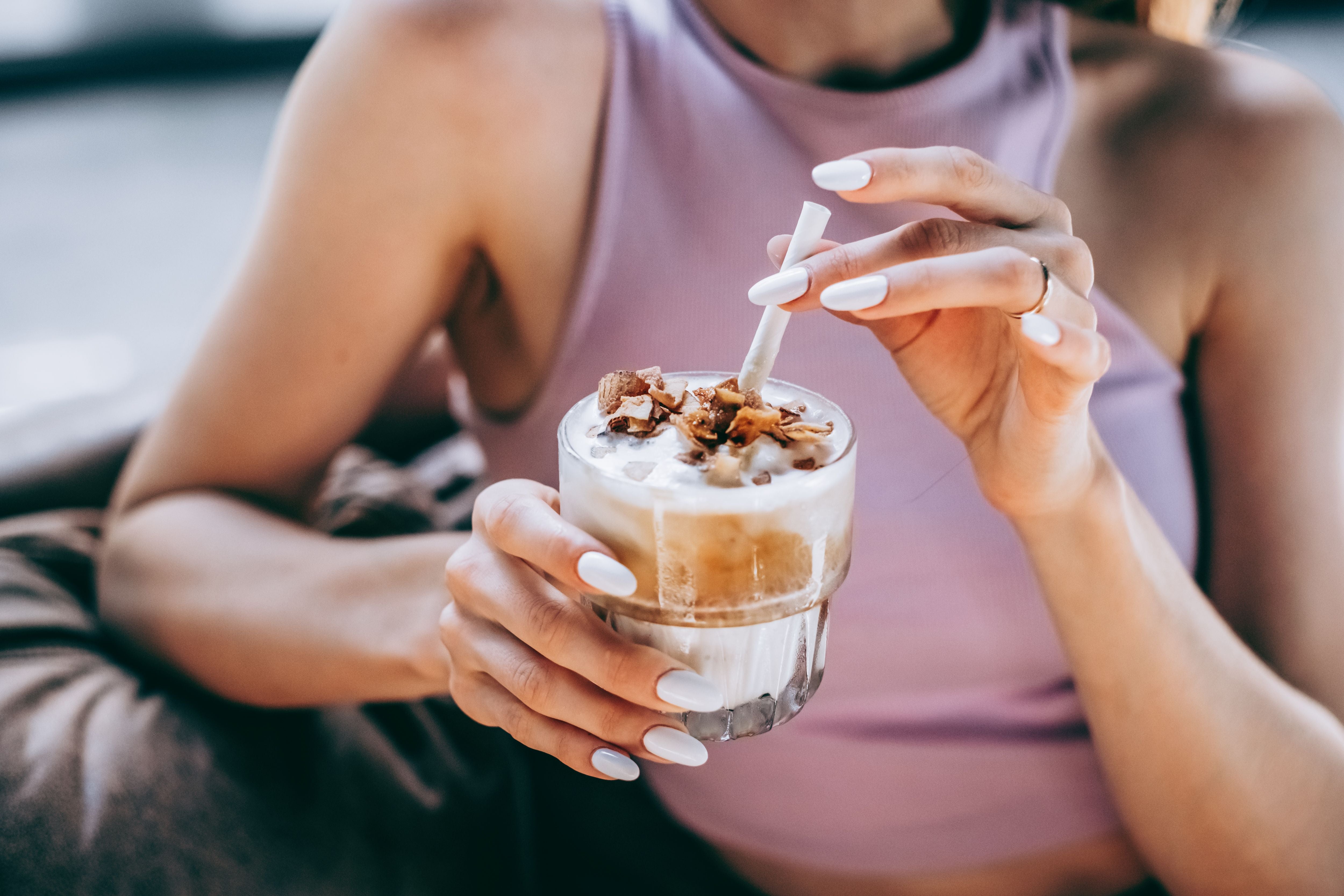 Frau hält ein Glas Eiskaffee mit Kokosflocken und trinkt mit einem weißen Strohhalm.