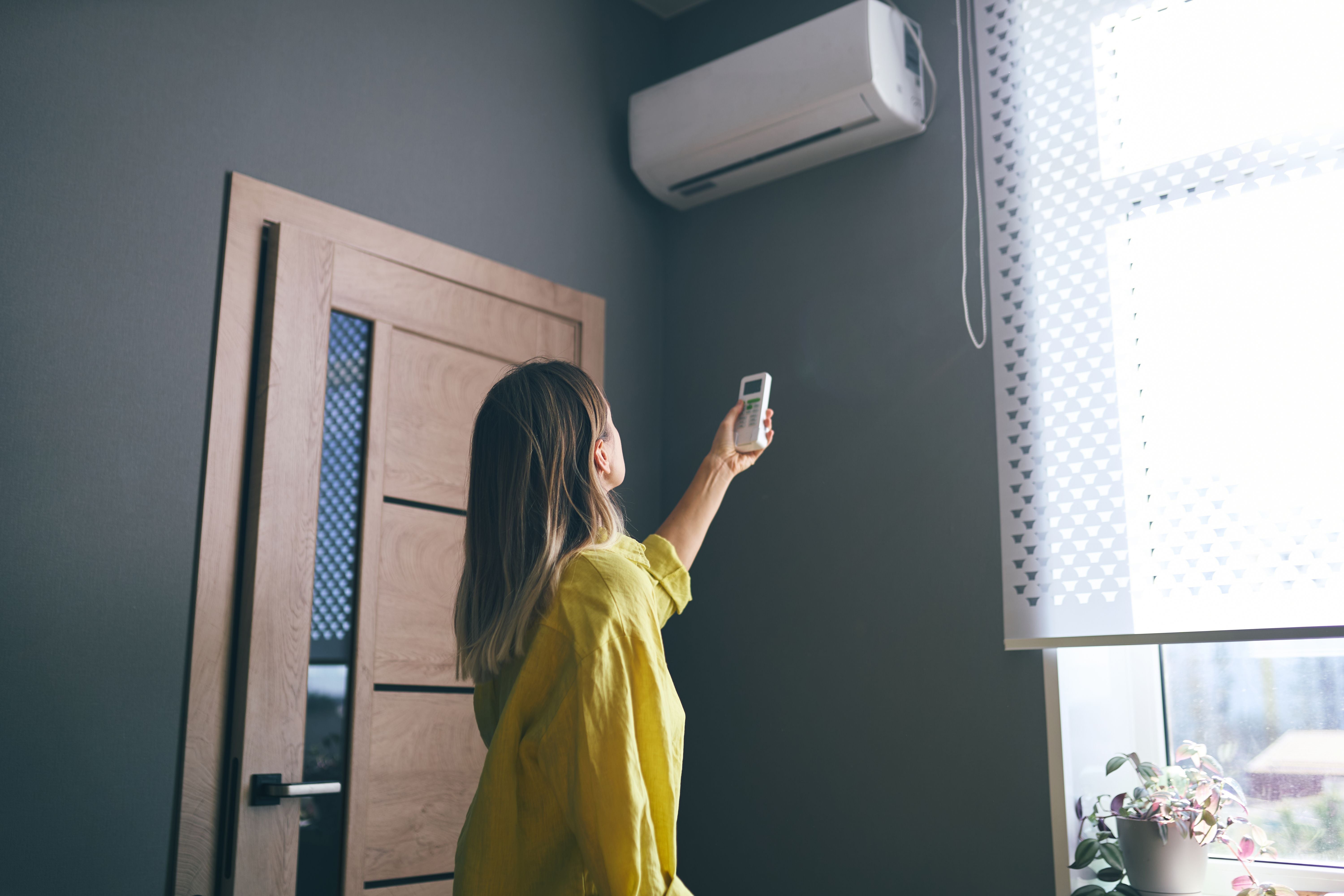 Frau schaltet mit Fernbedienung eine Klimaanlage in einem Zimmer ein.