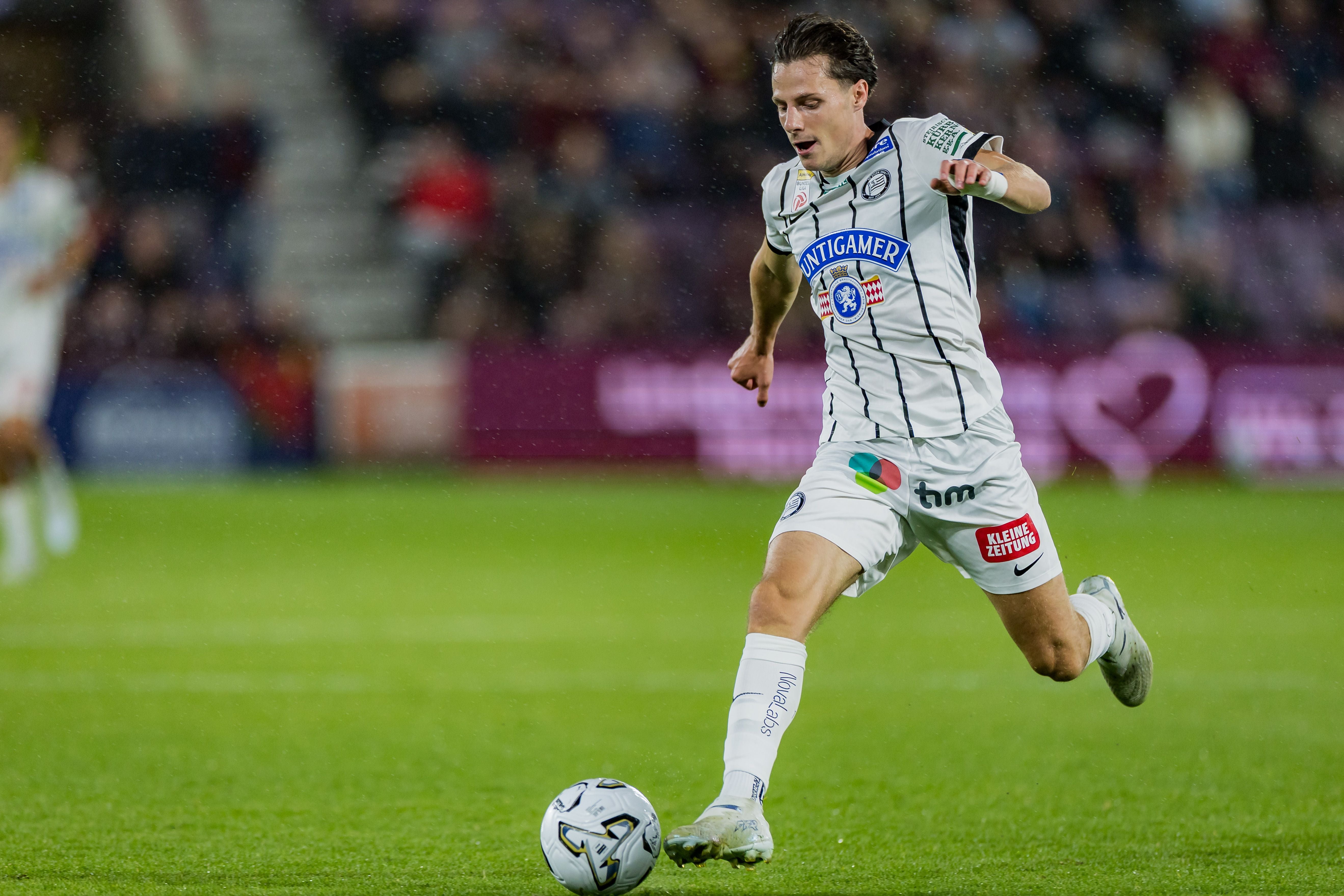 Ein Fußballspieler von Sturm Graz läuft im Stadion mit dem Ball am Fuß über das Spielfeld.