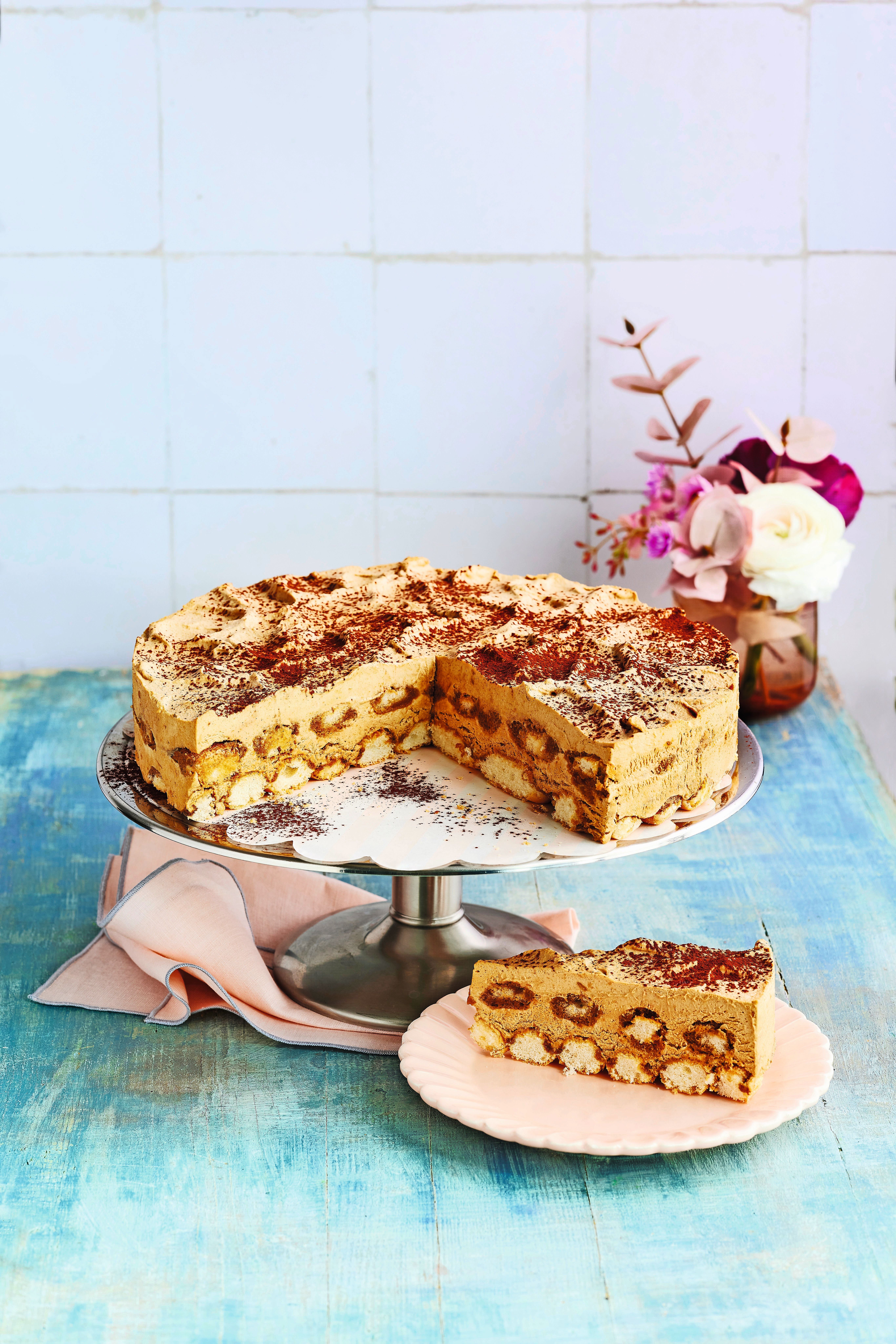Eiskaffee-Torte mit Löffelbiskuits auf Tortenplatte, ein Stück auf rosa Teller.