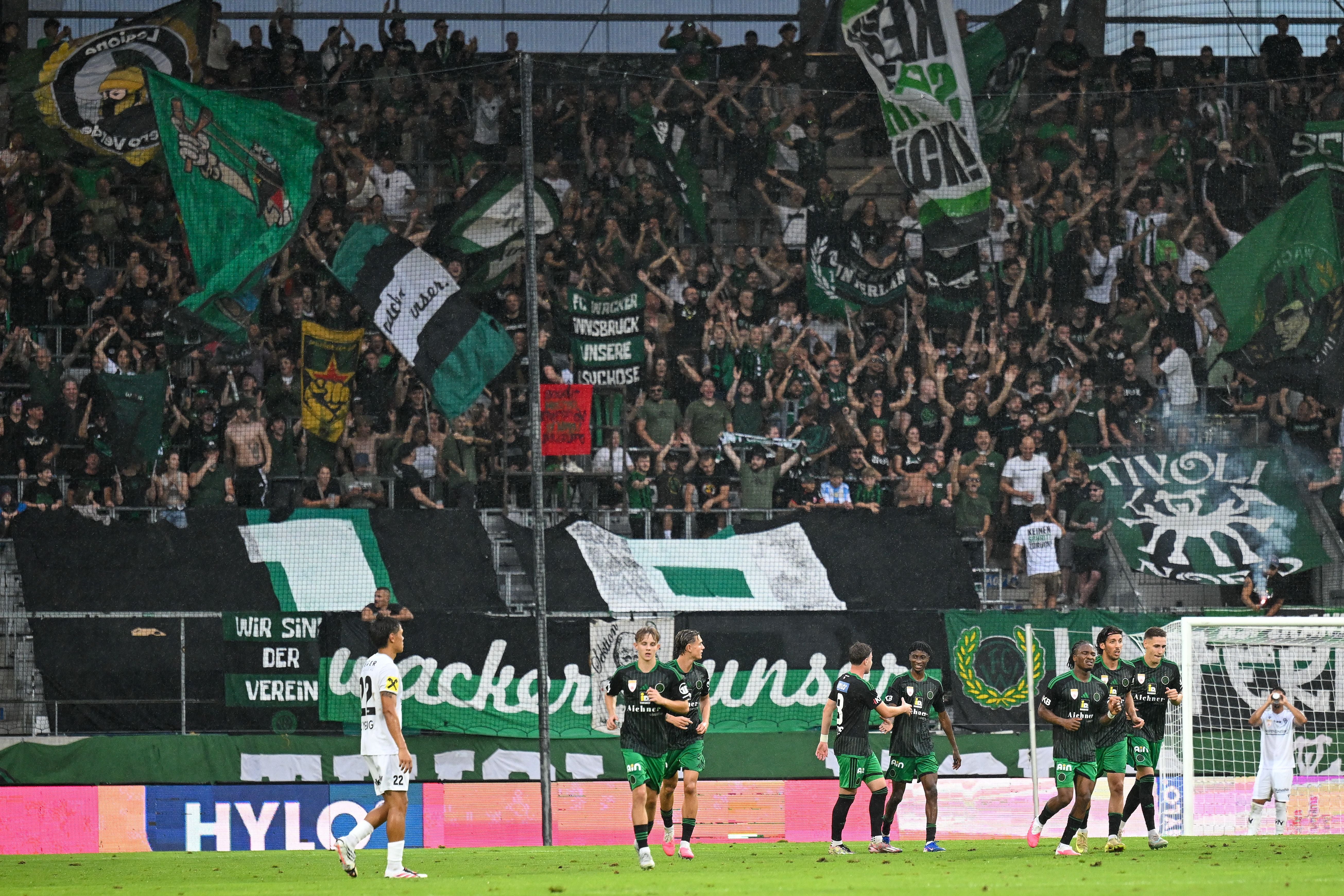 Fußballfans von Wacker Innsbruck jubeln mit Fahnen im Stadion.