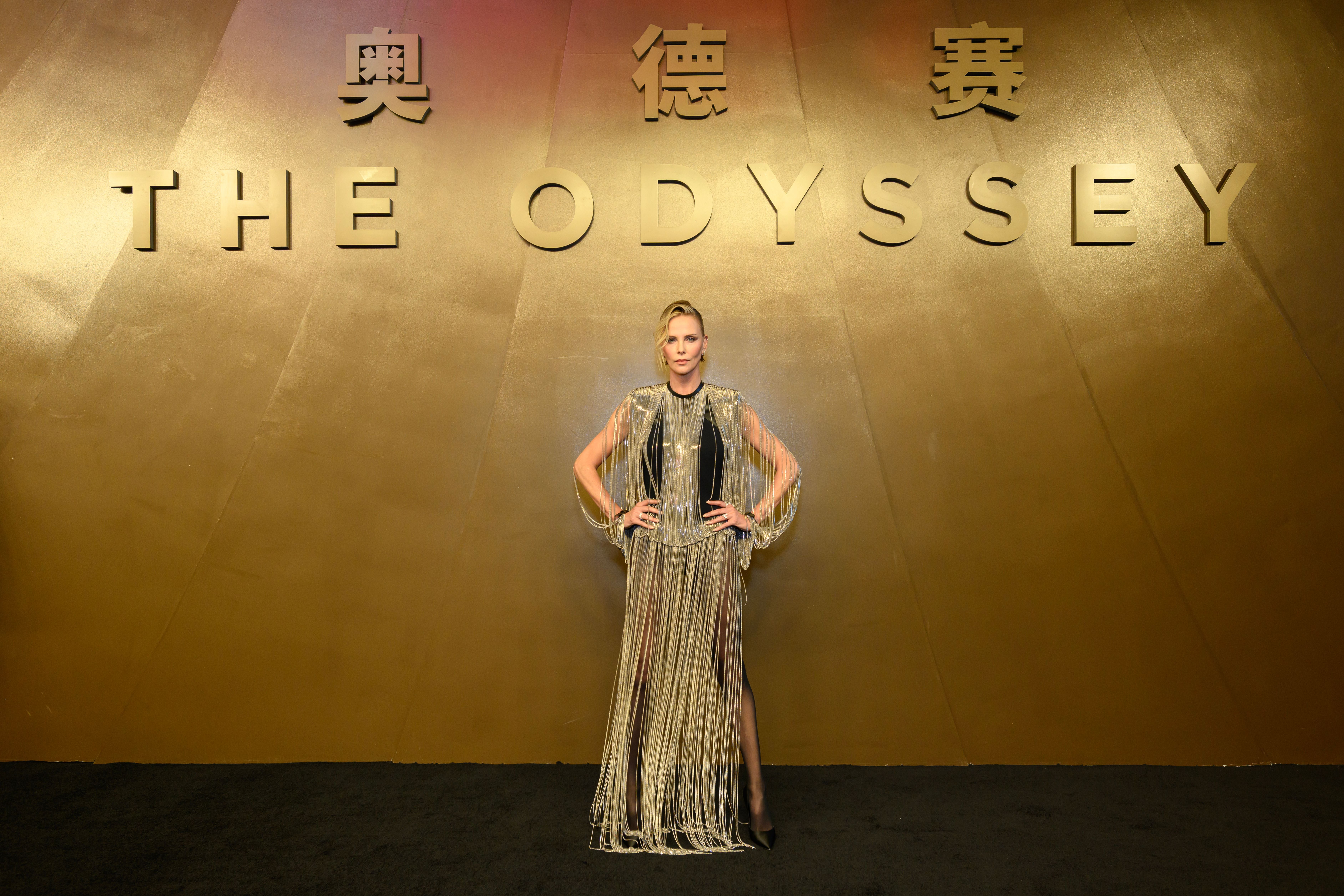 Frau in silbernem Kleid posiert vor goldener Wand mit Schriftzug "THE ODYSSEY" und chinesischen Zeichen.