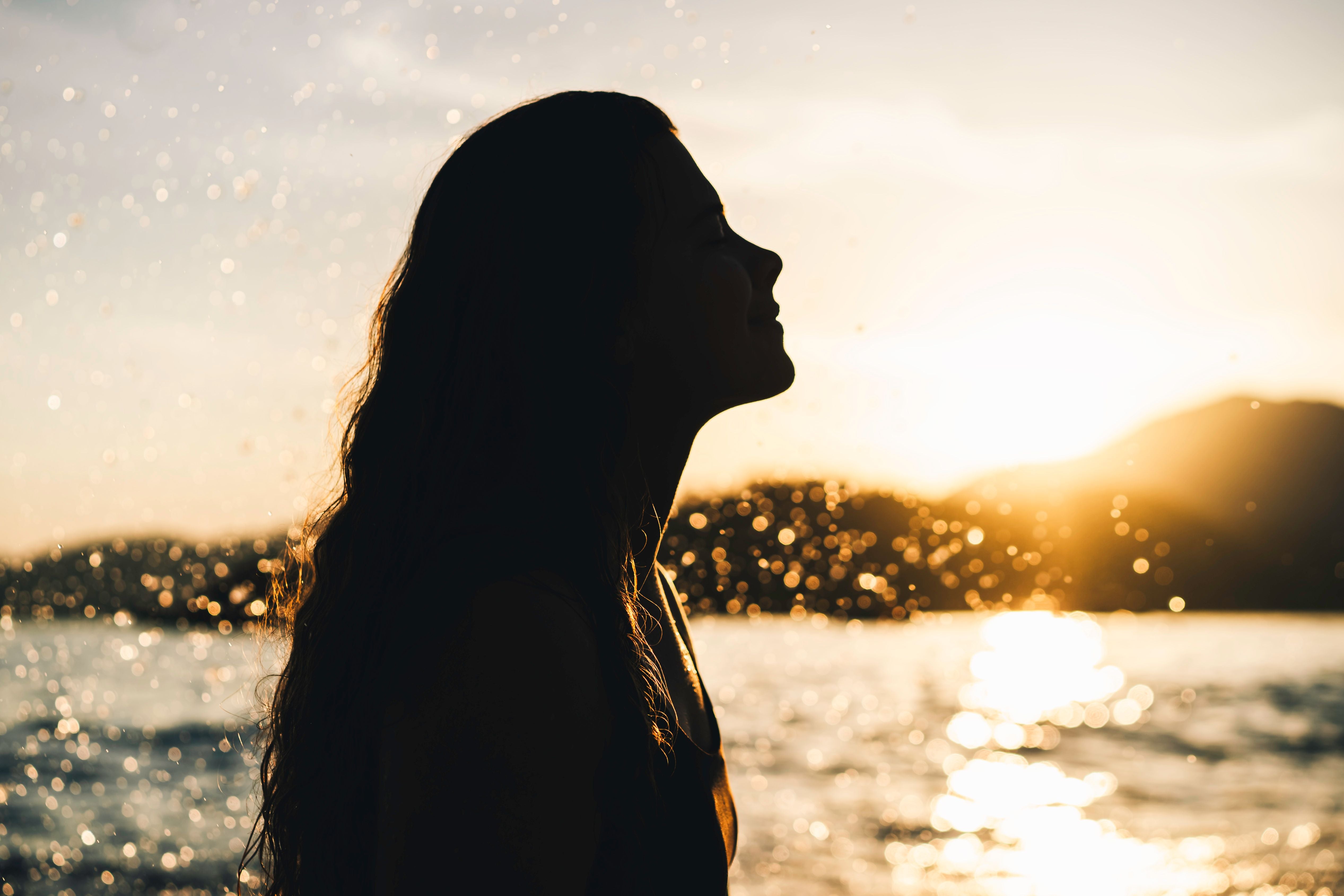 Silhouette einer Frau im Profil vor Sonnenuntergang am Wasser mit spritzenden Tropfen.