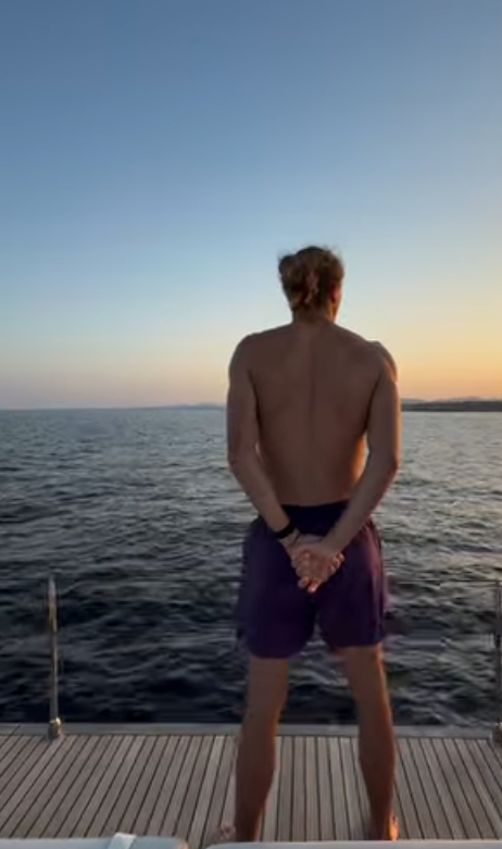 Eine Person steht barfuß auf einem Bootdeck und blickt aufs Meer bei Sonnenuntergang.