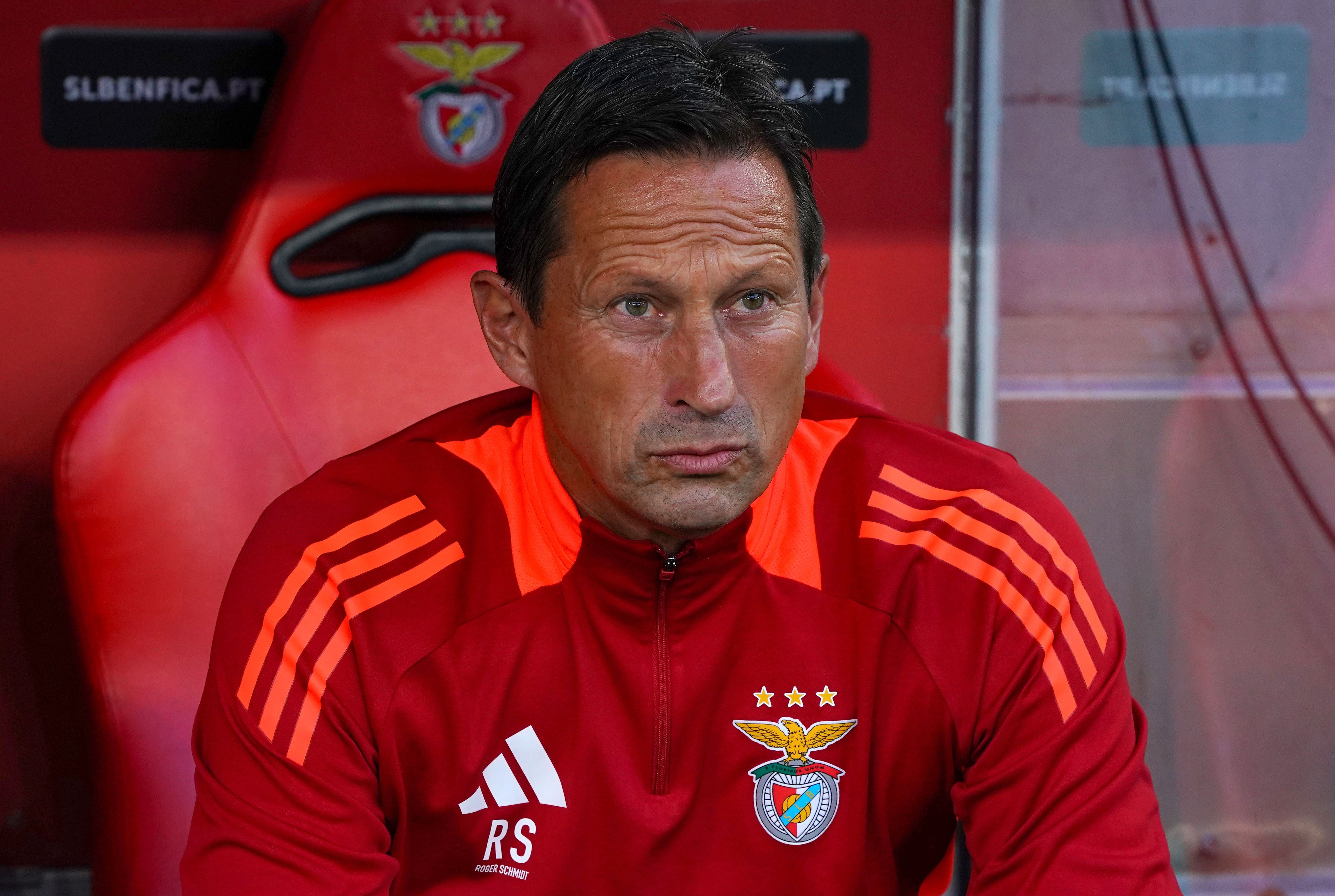 Ein Mann im roten Benfica-Trainingsanzug sitzt auf einer Trainerbank im Stadion.