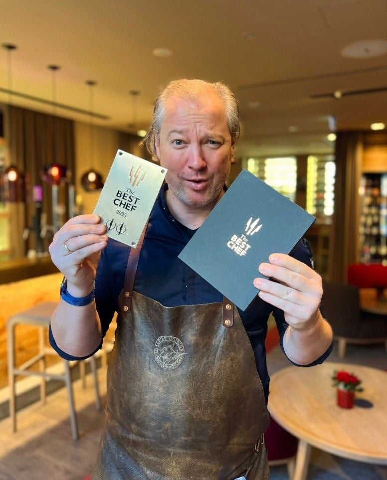 Ein Mann hält eine „The Best Chef 2025“-Auszeichnung und eine Urkunde in einem Restaurant.