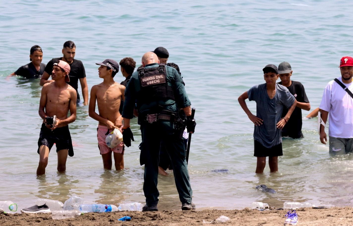 Ein spanischer Zivilgardist spricht am Strand mit einer Gruppe junger Migranten im Wasser.