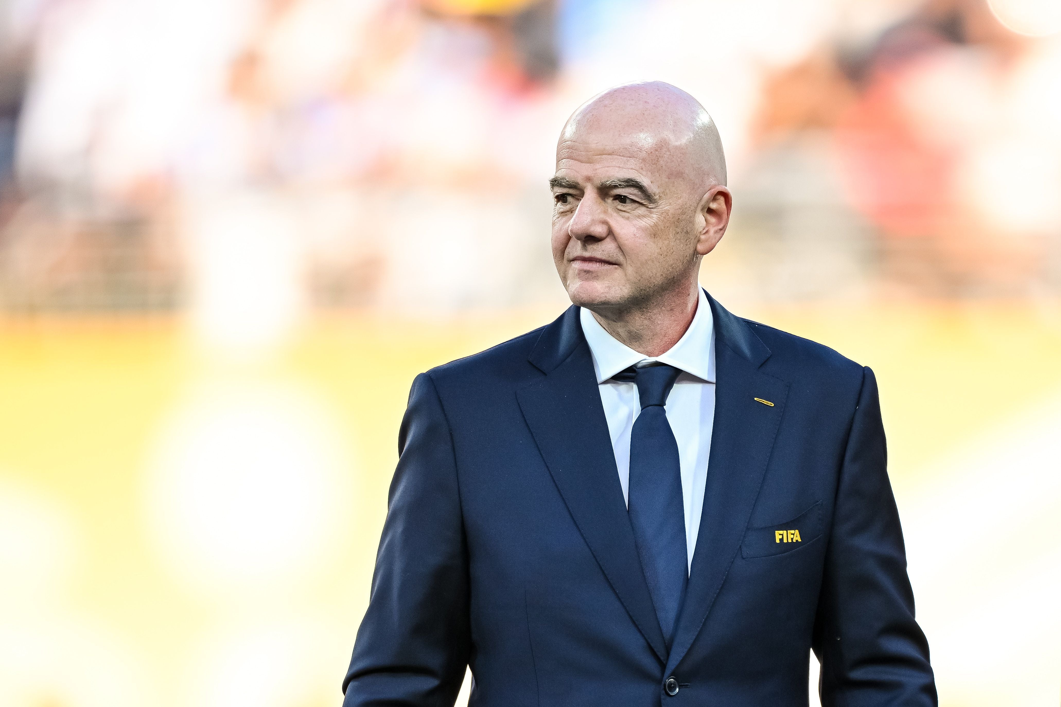 Ein Mann im Anzug mit FIFA-Logo steht vor unscharfem Hintergrund im Stadion.