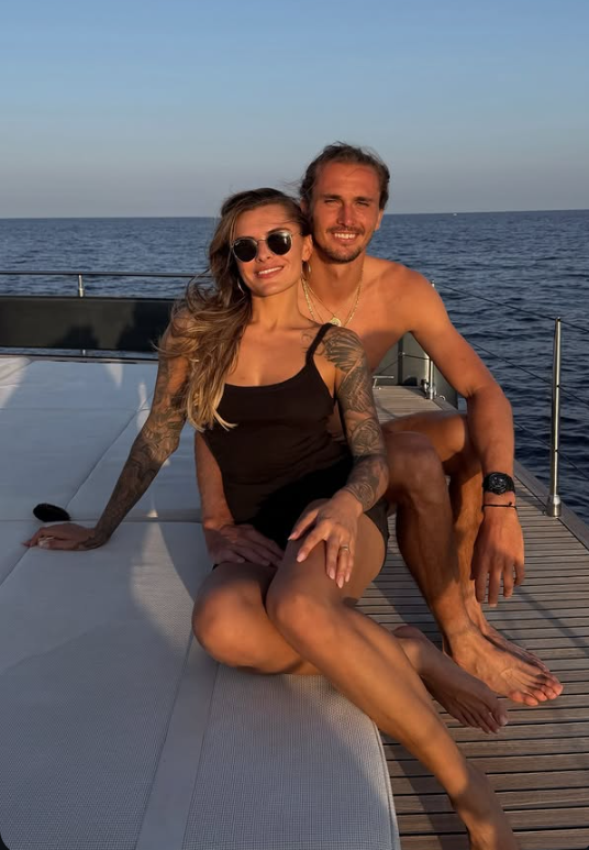 Ein Paar sitzt entspannt zusammen auf einer Yacht vor blauem Meer bei Sonnenuntergang.