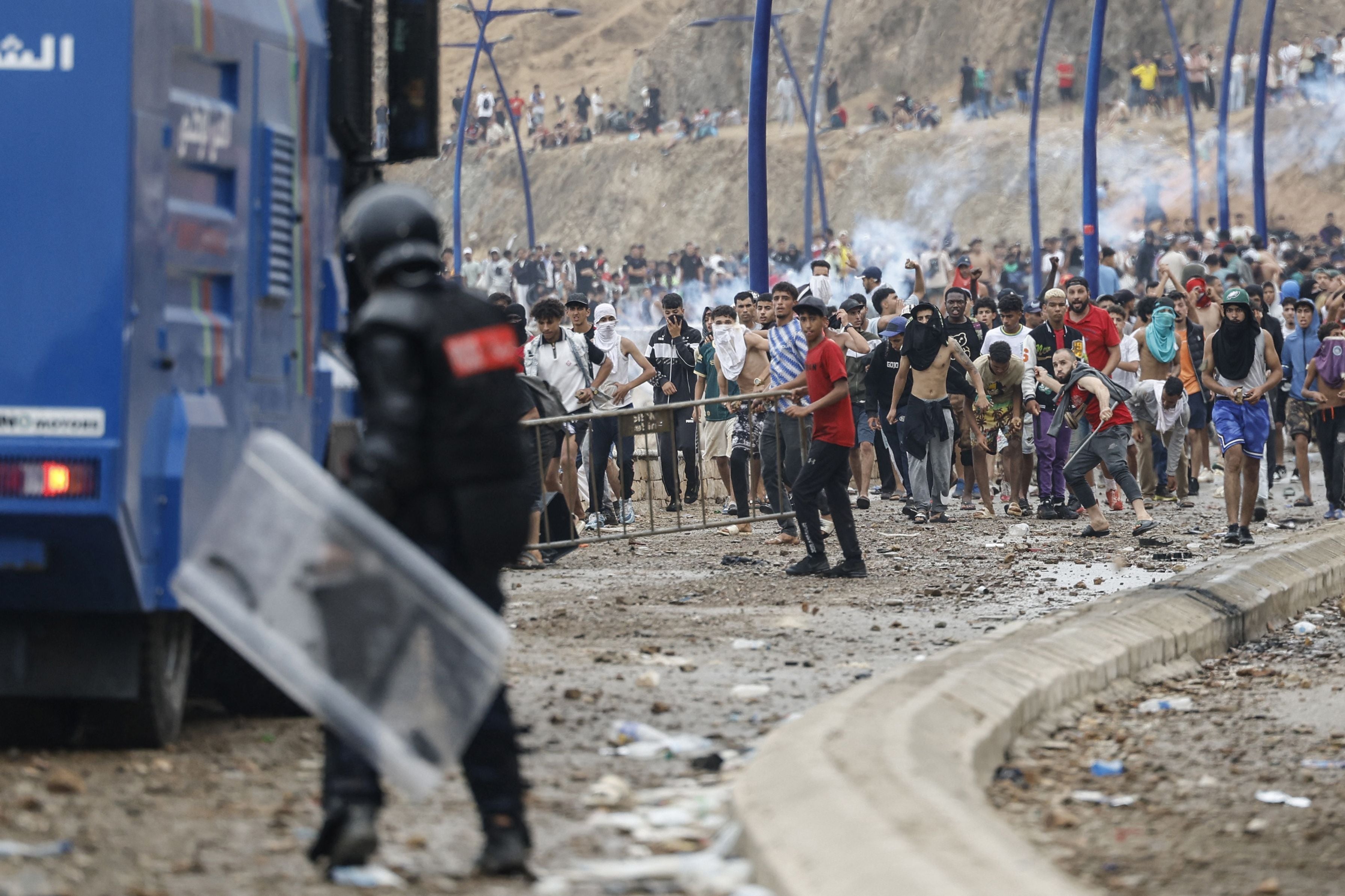 Polizisten in Schutzkleidung stehen Migranten gegenüber, die Steine werfen und Barrikaden errichten.