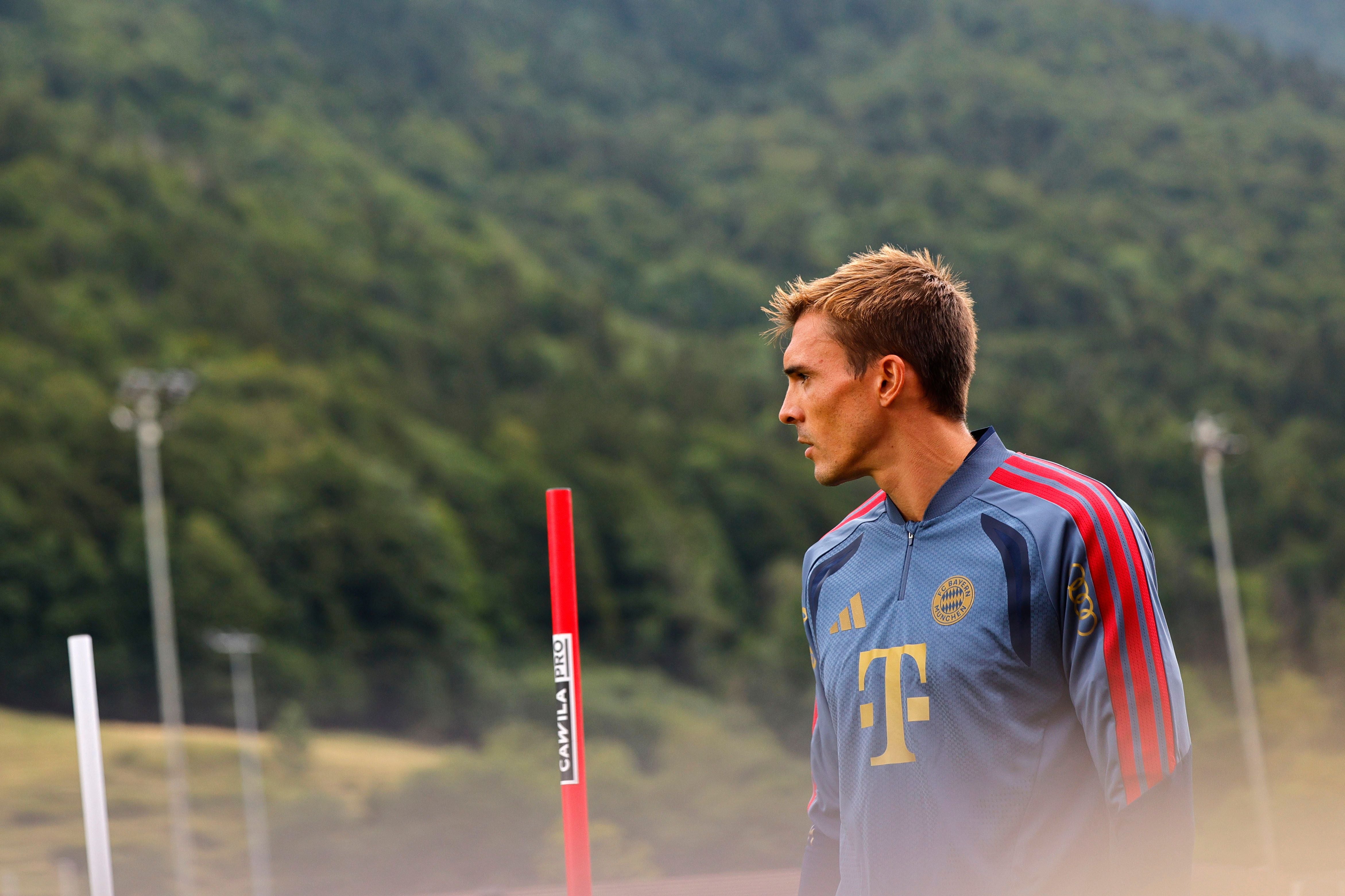 Ein Fußballspieler im Bayern-München-Trainingsanzug beim Training im Freien vor bewaldeten Hügeln.
