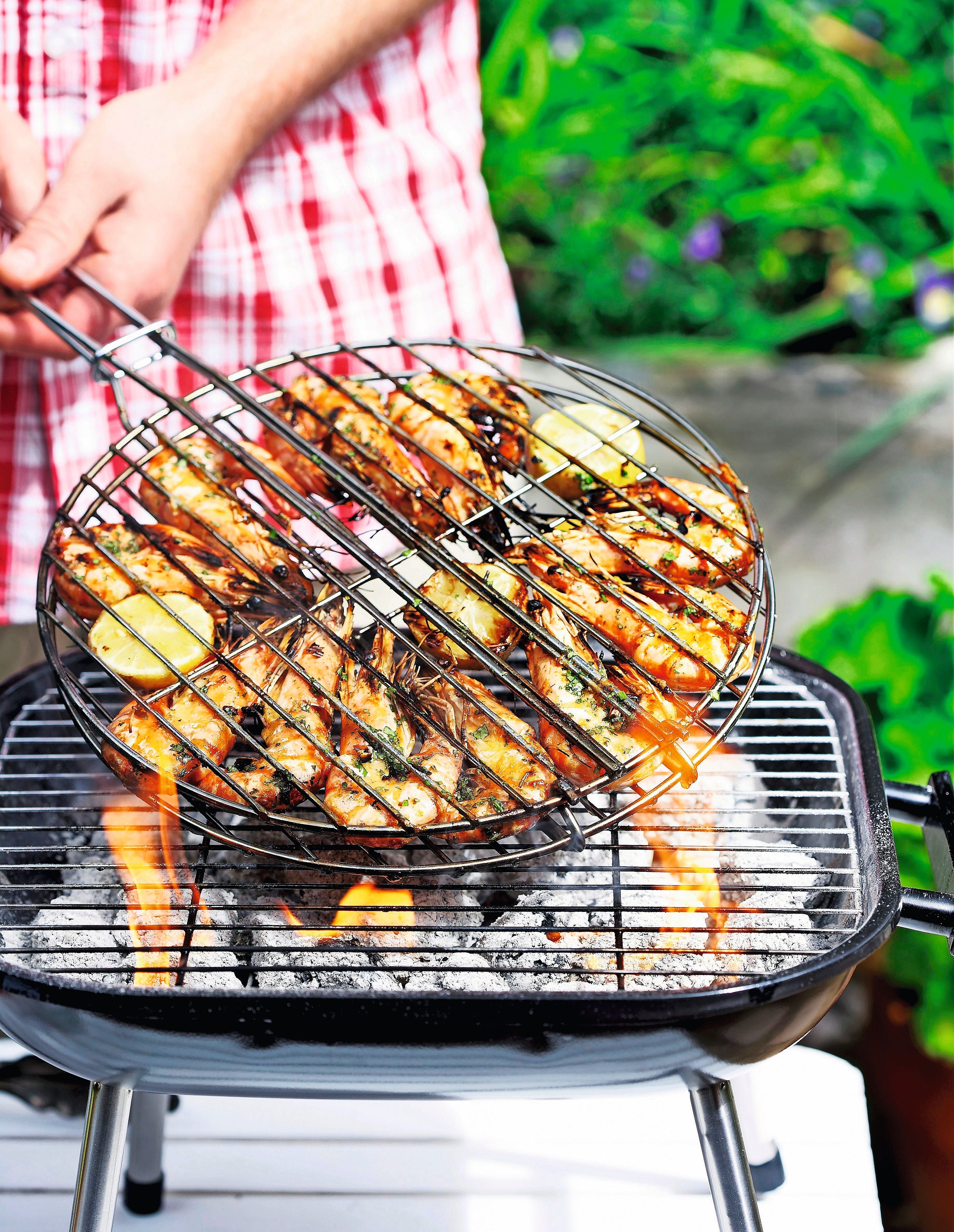Marinierte Garnelen werden auf einem Holzkohlegrill im Grillgitter gewendet.