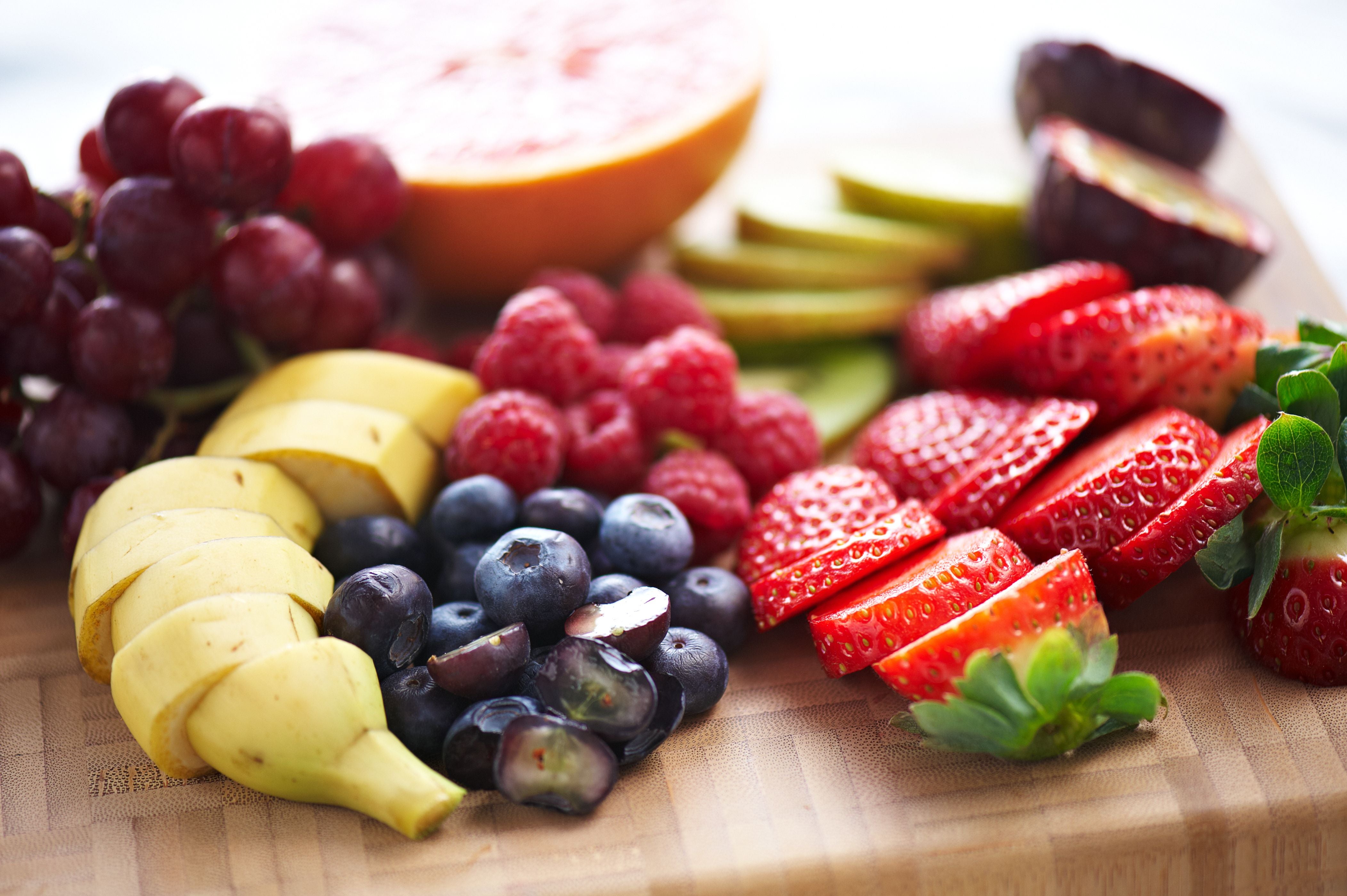 Verschiedene frische, geschnittene Früchte wie Erdbeeren, Banane, Trauben und Beeren auf Holzbrett.