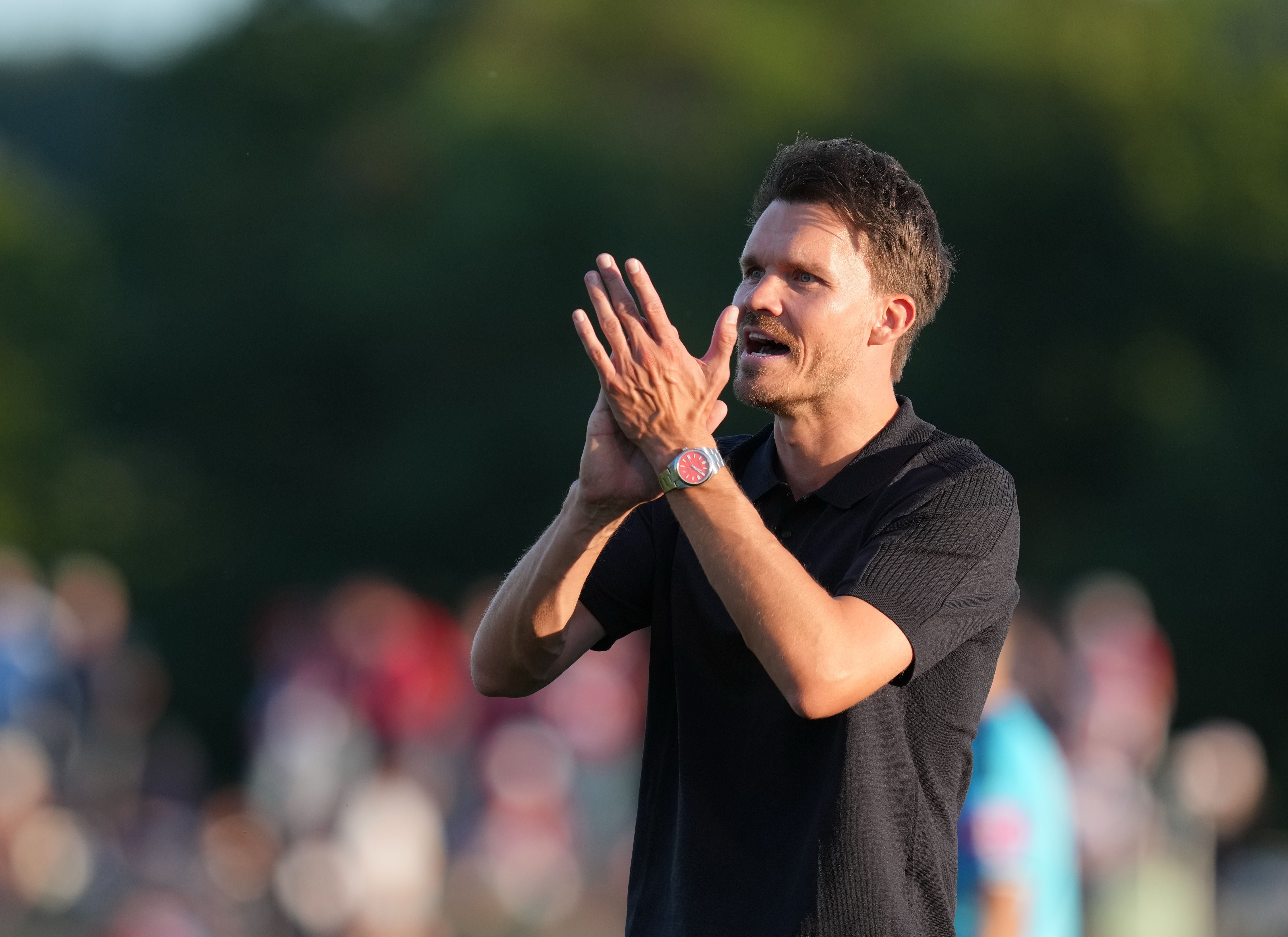 Ein Mann im schwarzen Polohemd klatscht und ruft auf einem Sportplatz.