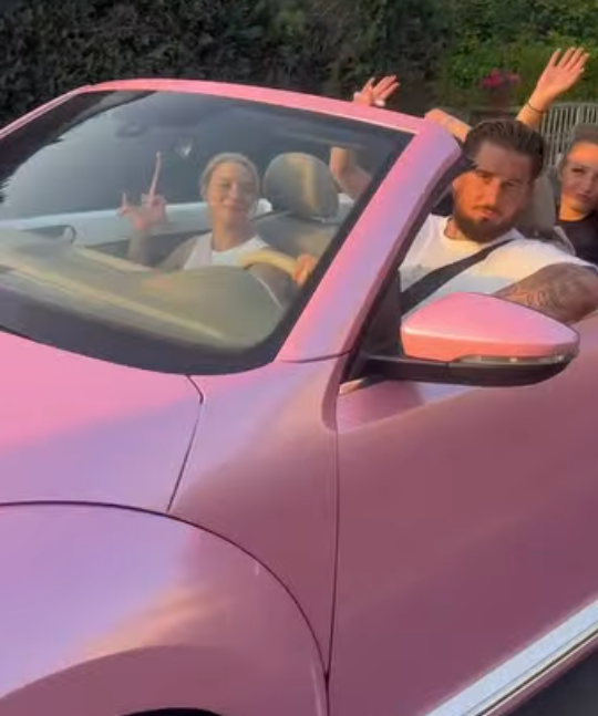 Vier Personen sitzen fröhlich in einem pinken Cabrio, zwei heben die Arme zum Gruß.