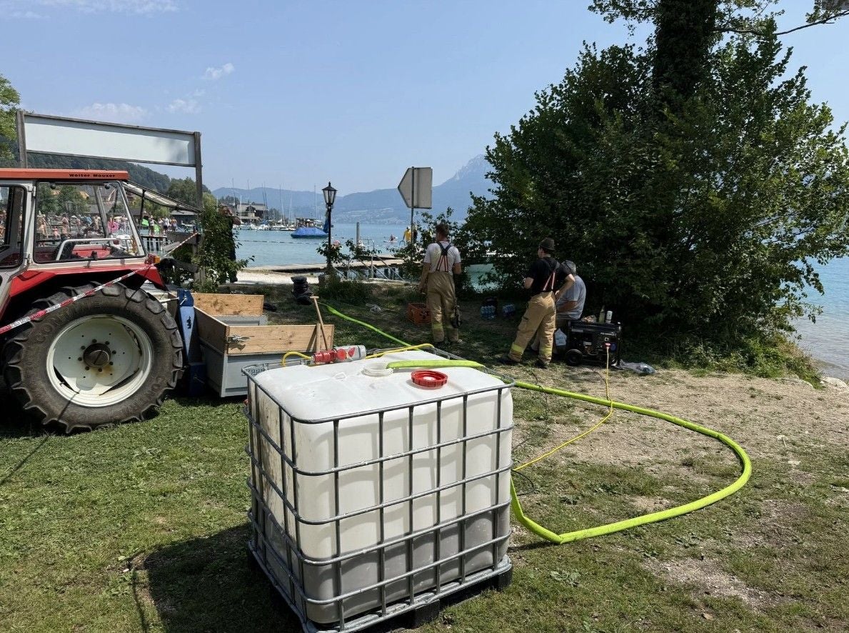 Feuerwehrleute arbeiten mit Ausrüstung und Wassertank am Ufer des Attersees.