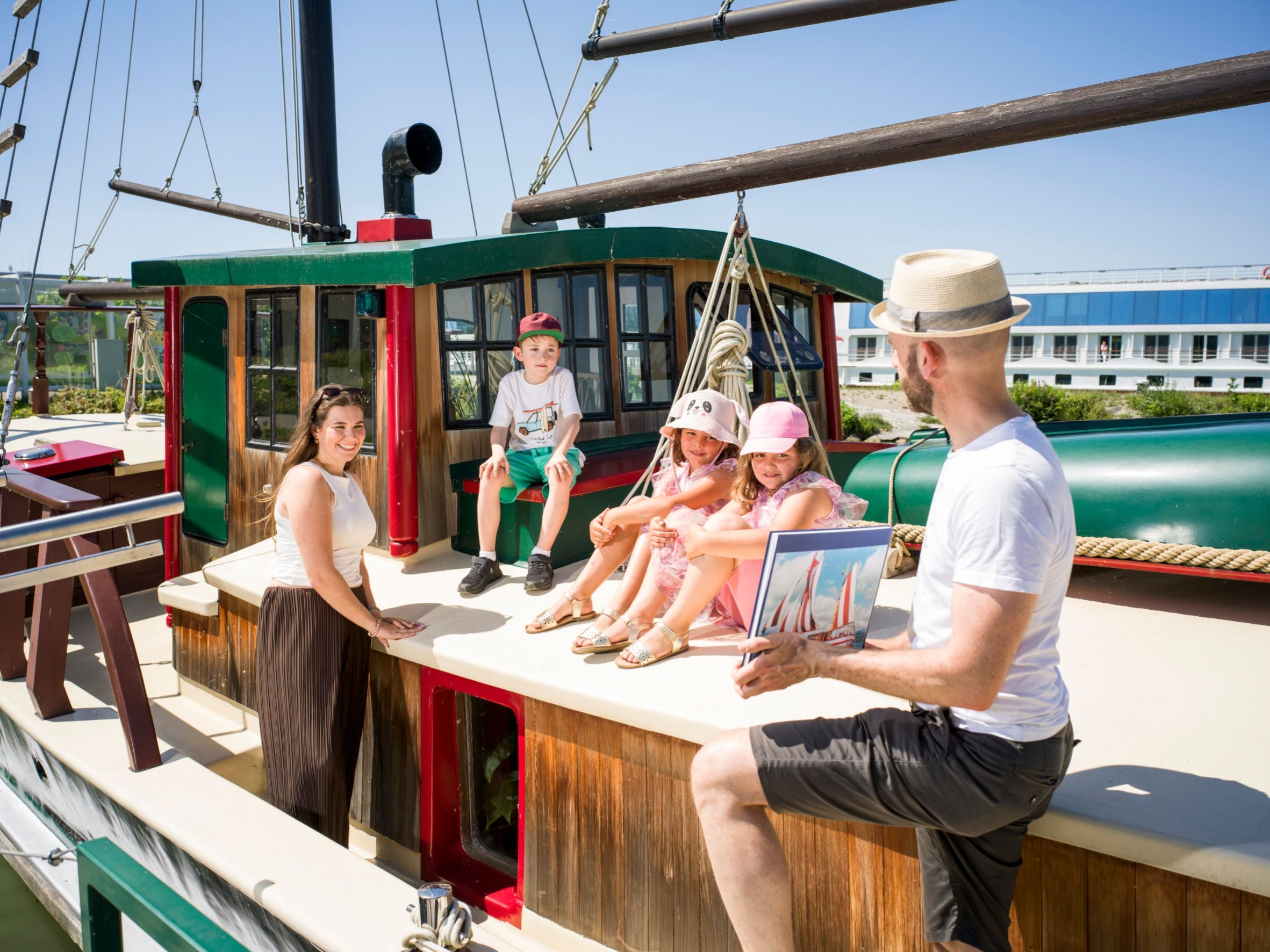 Eine Familie sitzt fröhlich auf einem Holzschiff mit Sonnenschein und blauem Himmel.