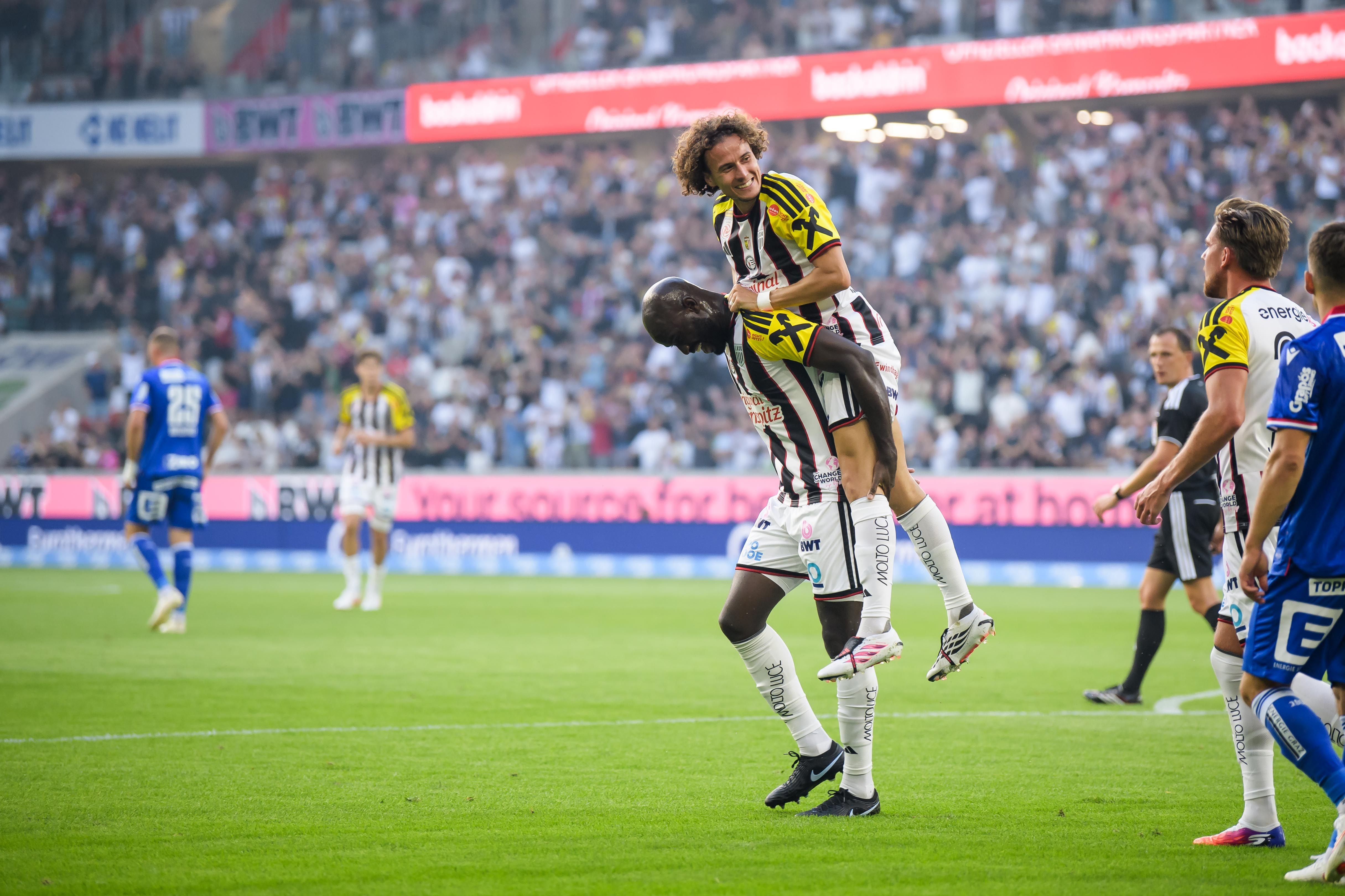 Zwei LASK-Spieler jubeln auf dem Fußballfeld, einer hebt den anderen hoch.