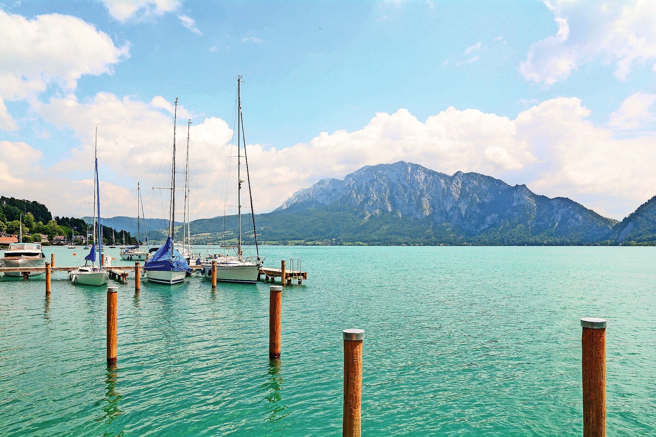 Segelboote liegen am Steg auf dem türkisgrünen Attersee vor Alpen-Bergkulisse.
