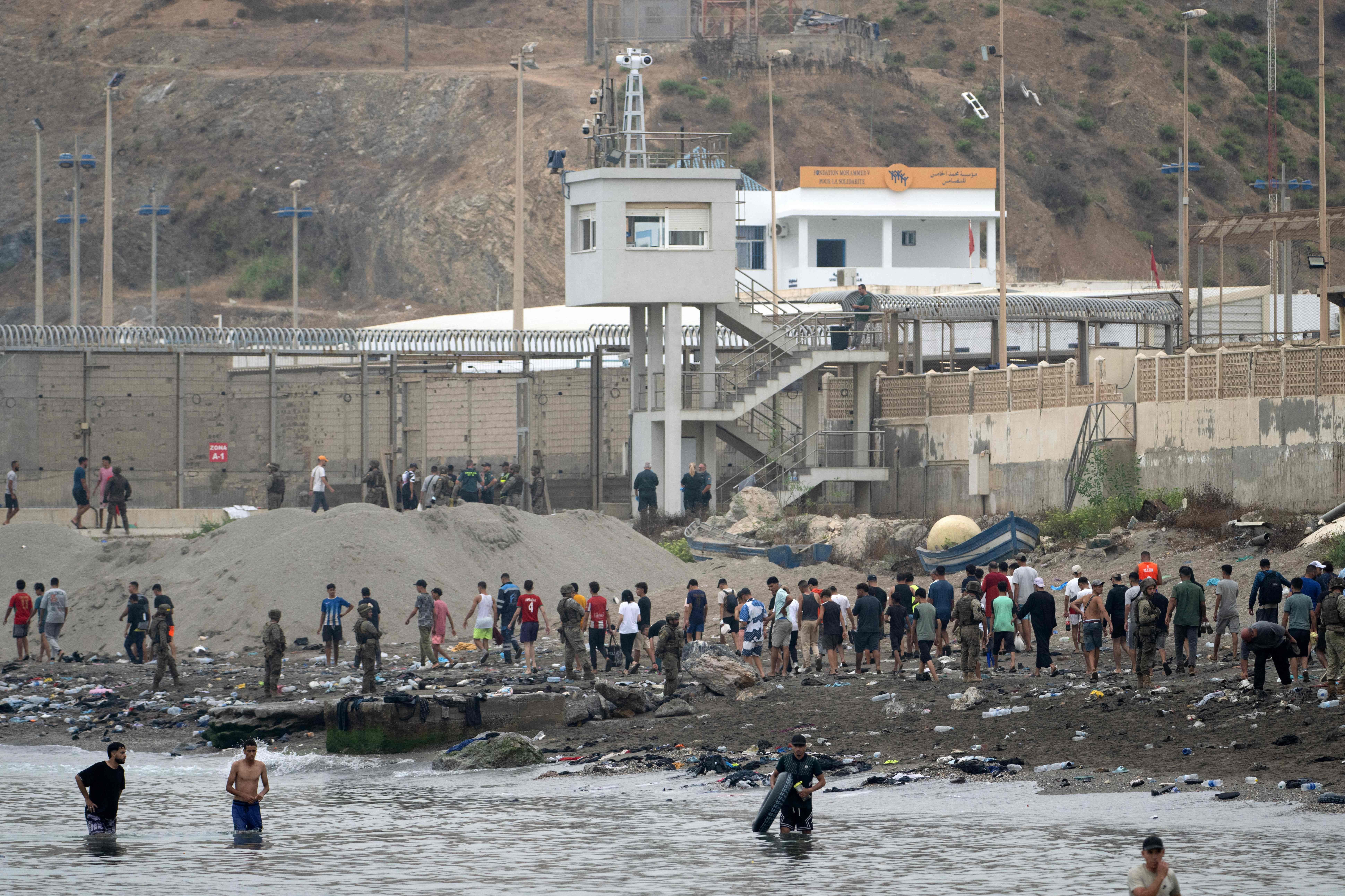 Viele Menschen stehen und waten am Strand und im Wasser nahe eines Grenzzauns zwischen Marokko und Ceuta.
