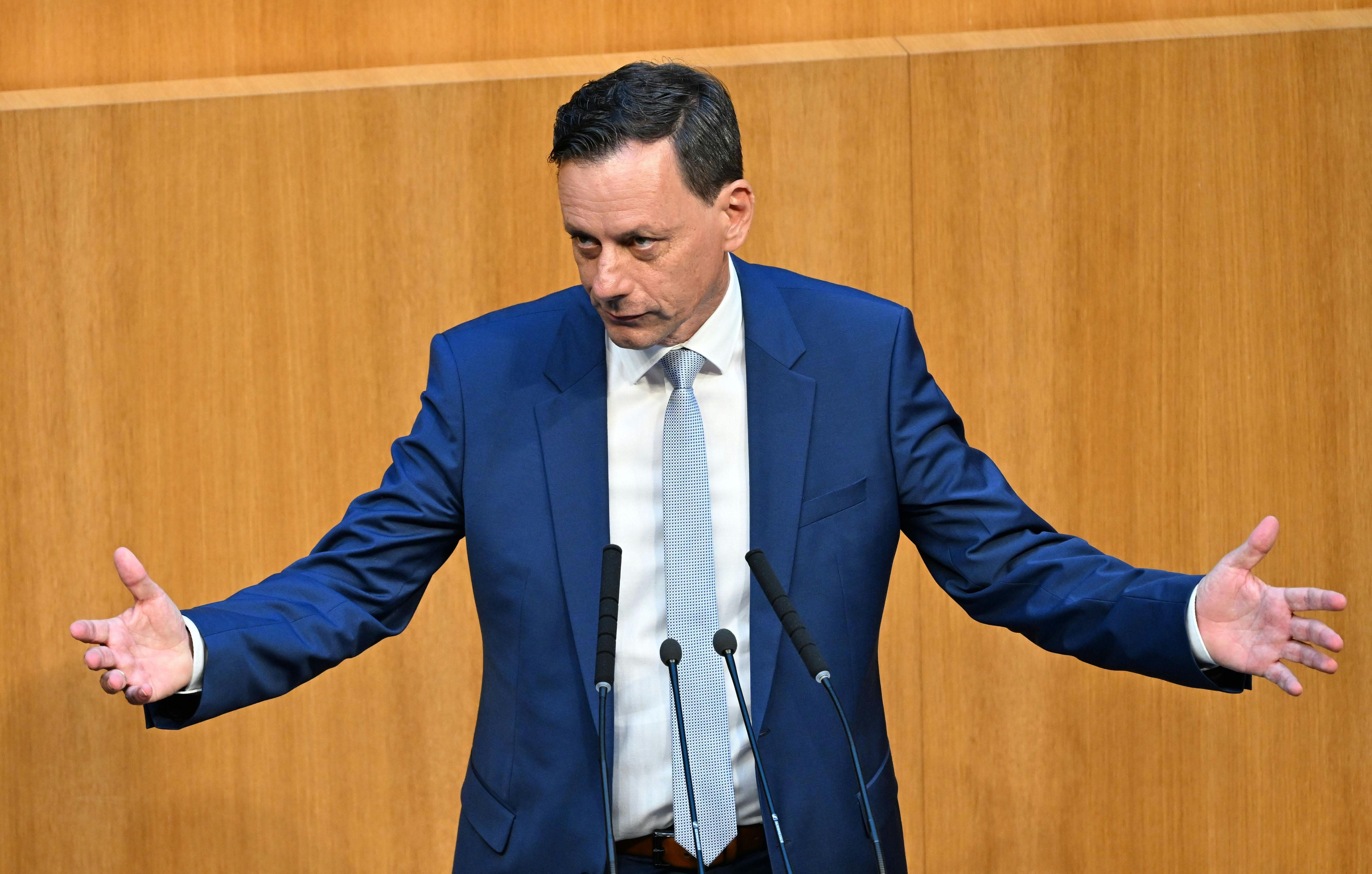 Ein Mann im blauen Anzug spricht gestikulierend an einem Rednerpult im Parlament.