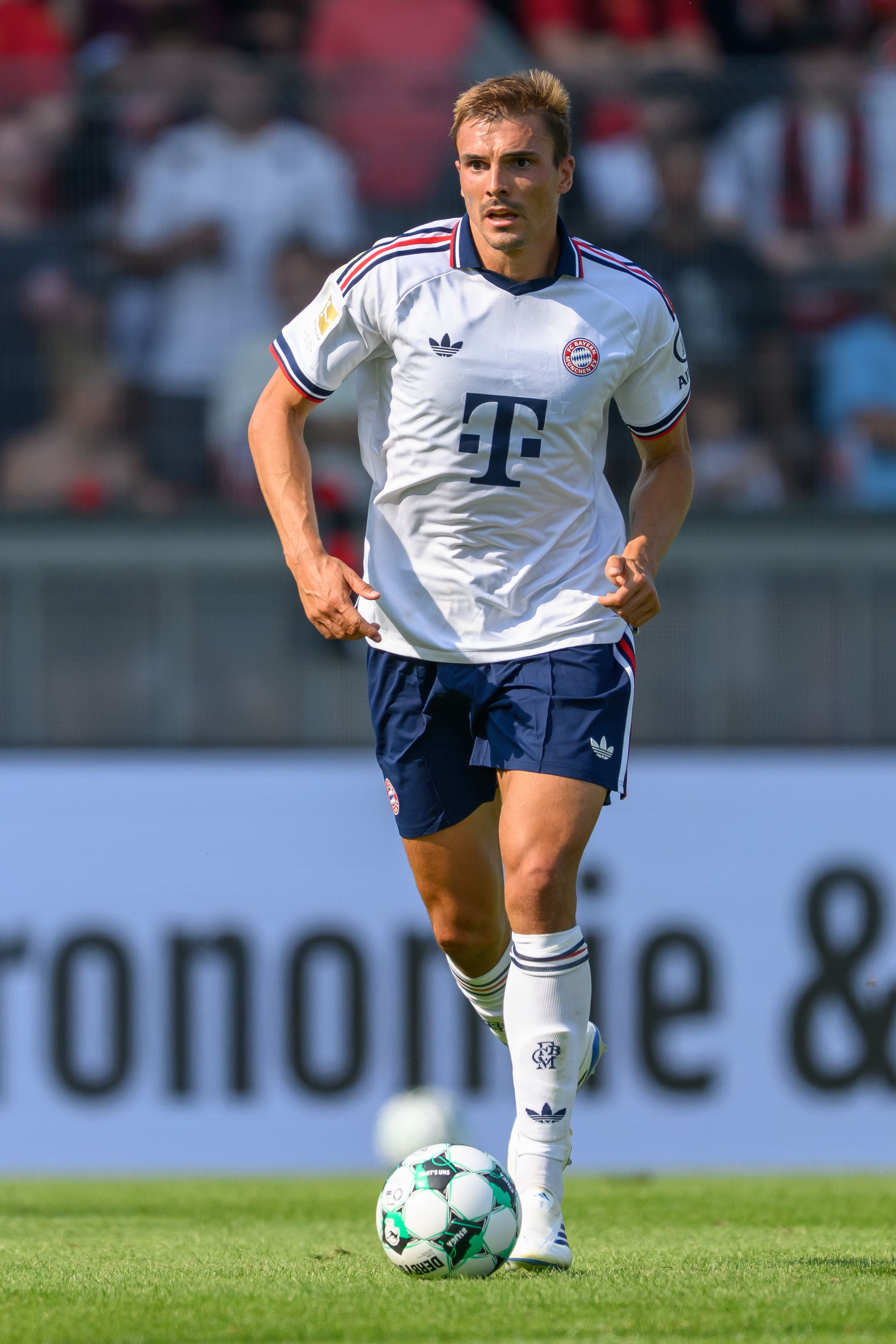Ein Fußballspieler von Bayern München läuft im weißen Trikot mit Ball auf dem Spielfeld.
