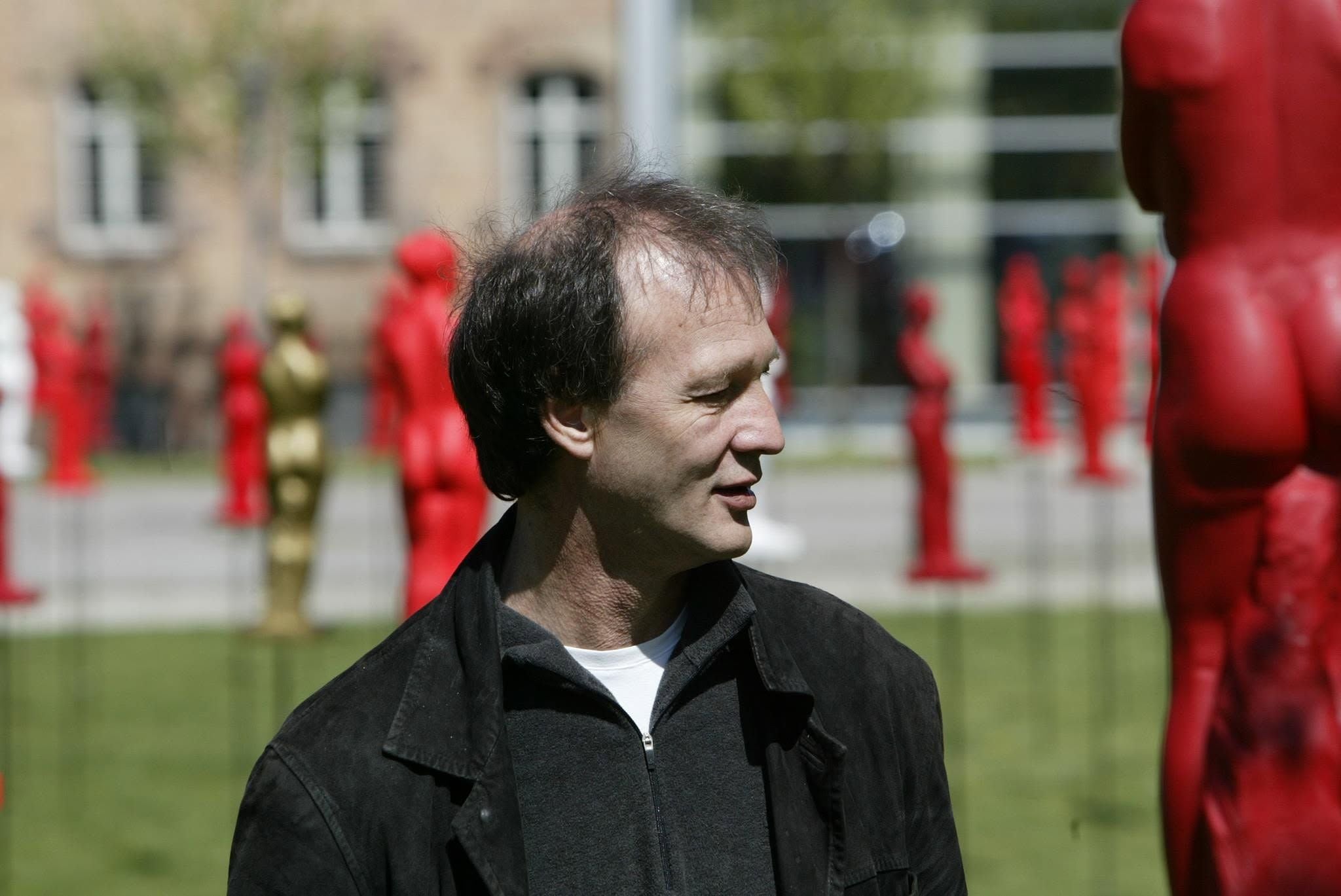 Ein Mann steht im Freien zwischen zahlreichen roten und goldenen Figuren.