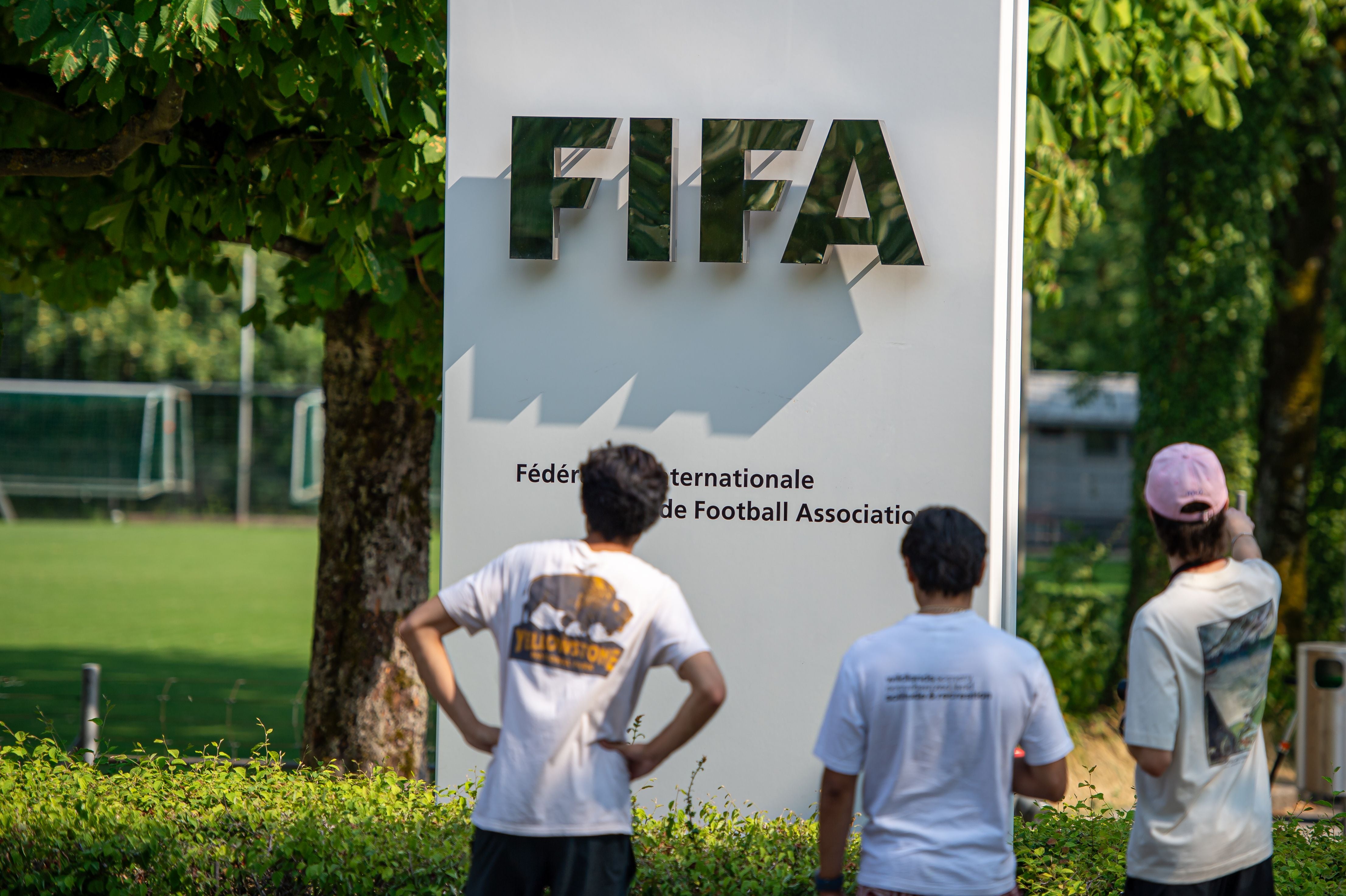 Drei Personen stehen vor einem FIFA-Schild am Hauptsitz in Zürich im Grünen.