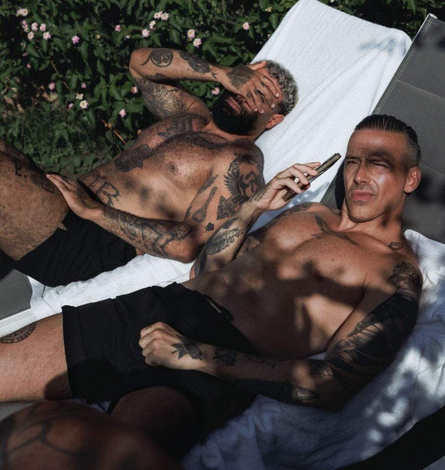 Zwei tätowierte Männer liegen in Shorts auf Sonnenliegen und entspannen im Freien.