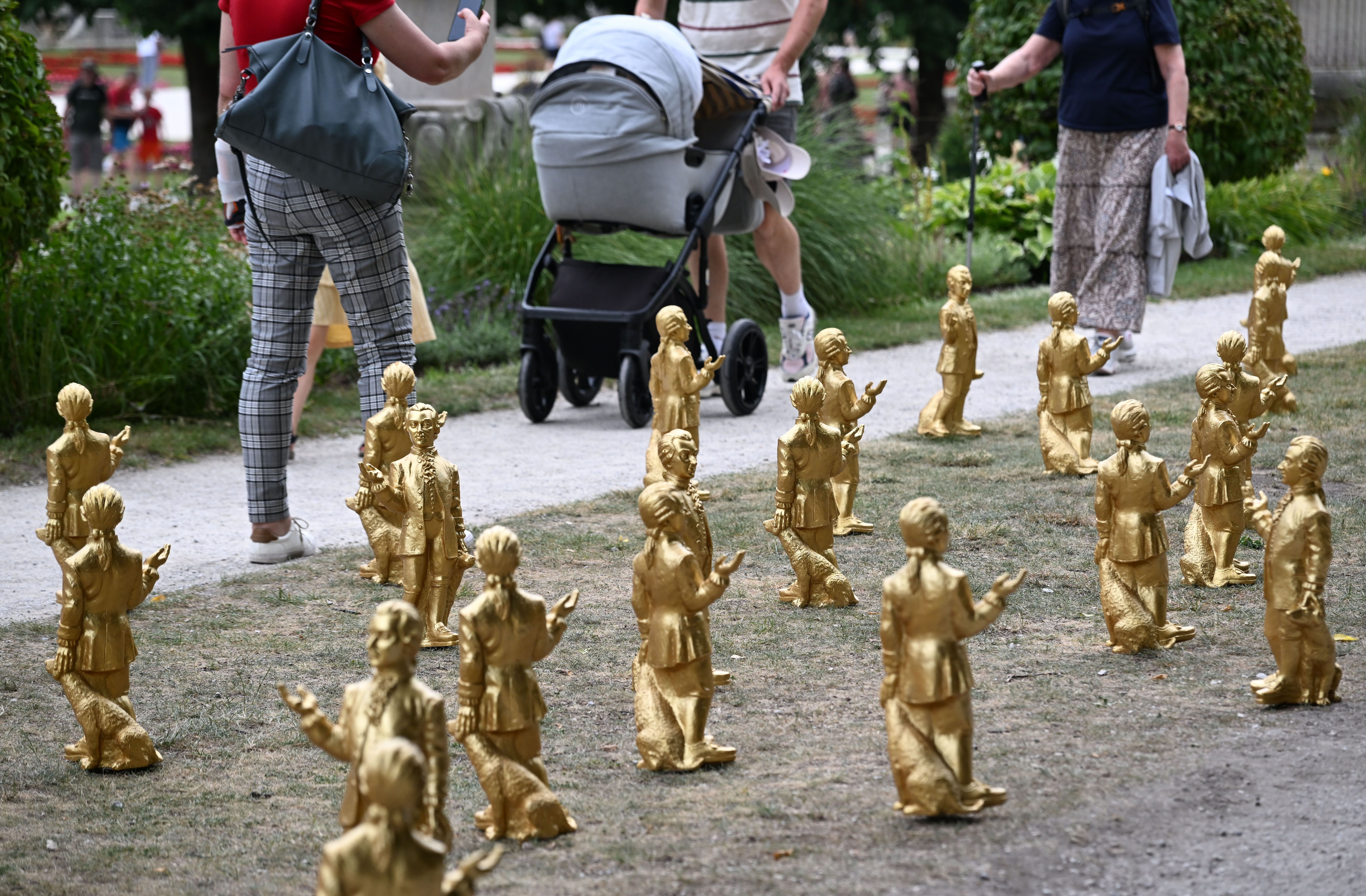 Viele goldene Mozart-Figuren stehen auf dem Rasen im Mirabellgarten, Menschen gehen vorbei.