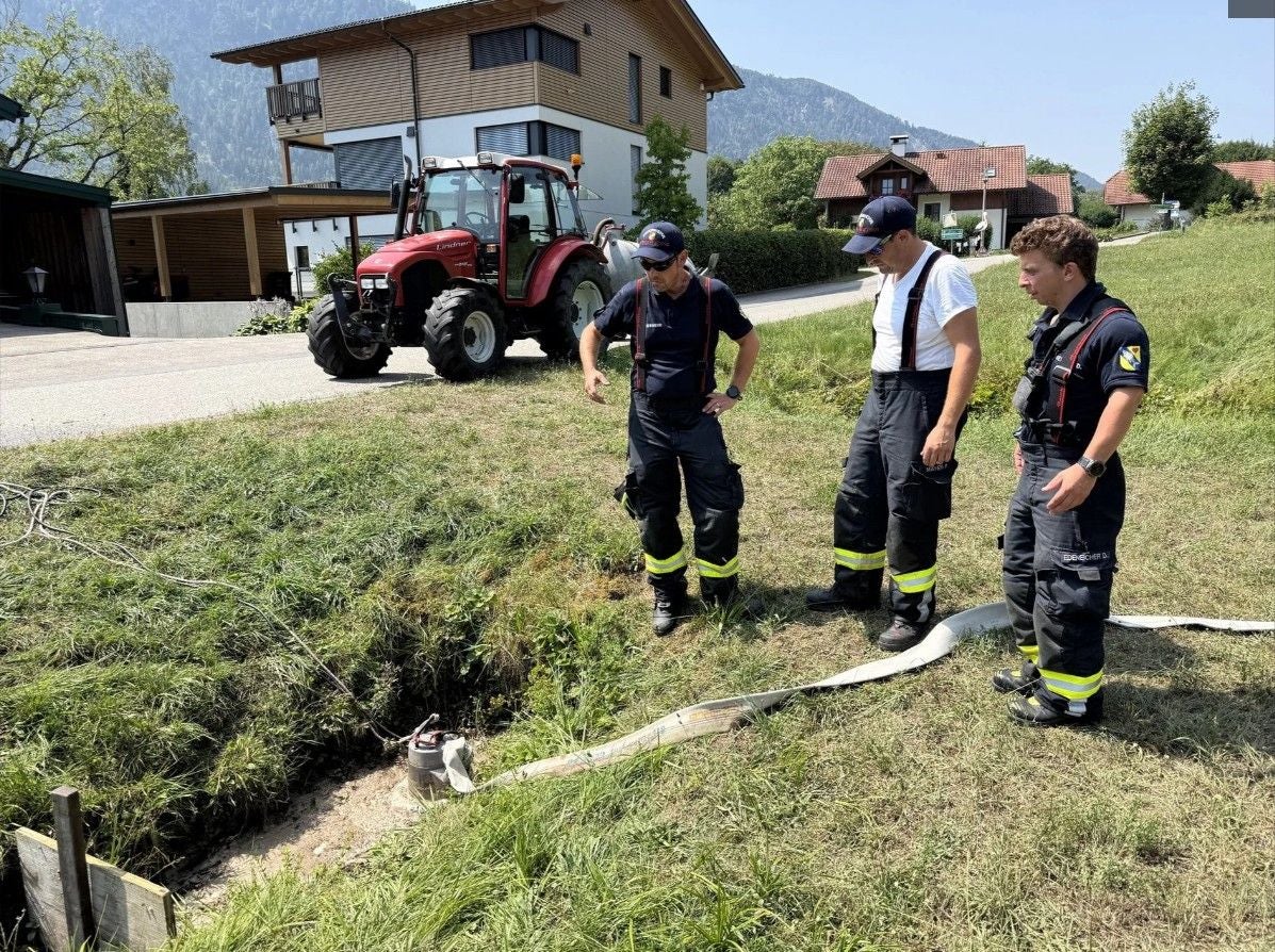 Drei Einsatzkräfte begutachten eine Pumpe in einem Graben, im Hintergrund steht ein Traktor.