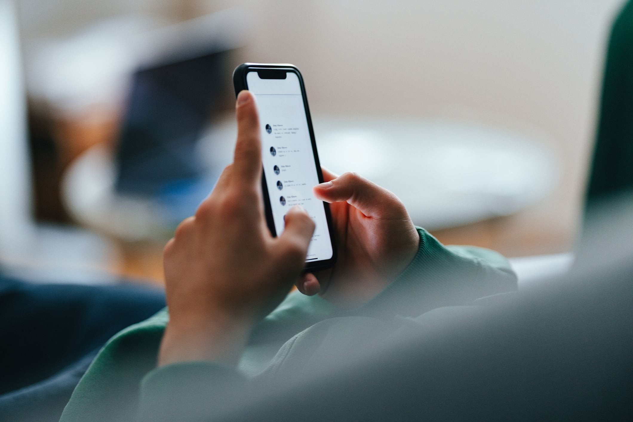 Jugendlicher tippt Nachrichten auf seinem Smartphone, während er auf einem Sofa liegt.