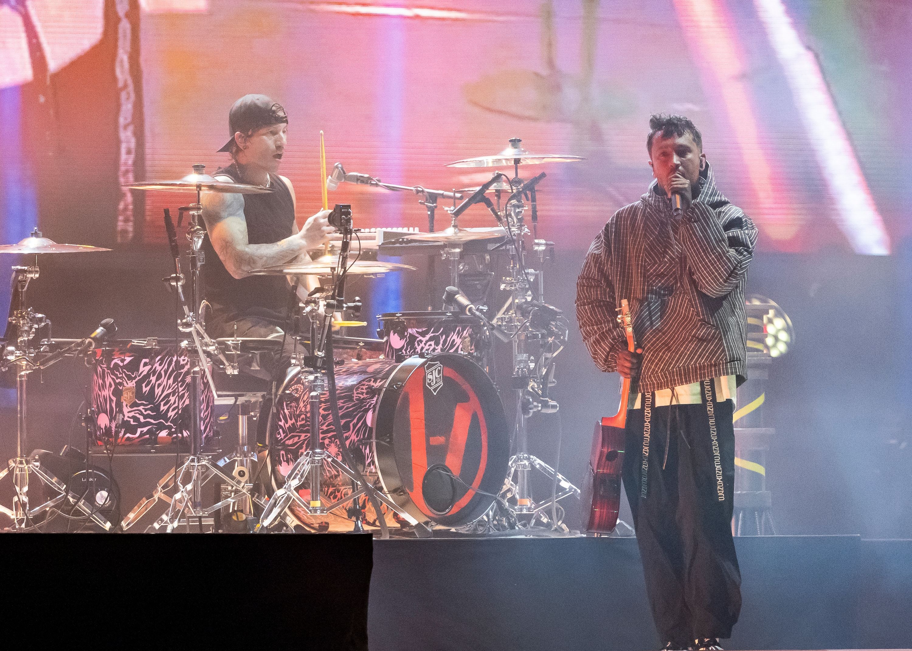 Zwei Musiker von Twenty One Pilots stehen auf einer Bühne, einer spielt Schlagzeug, der andere singt.