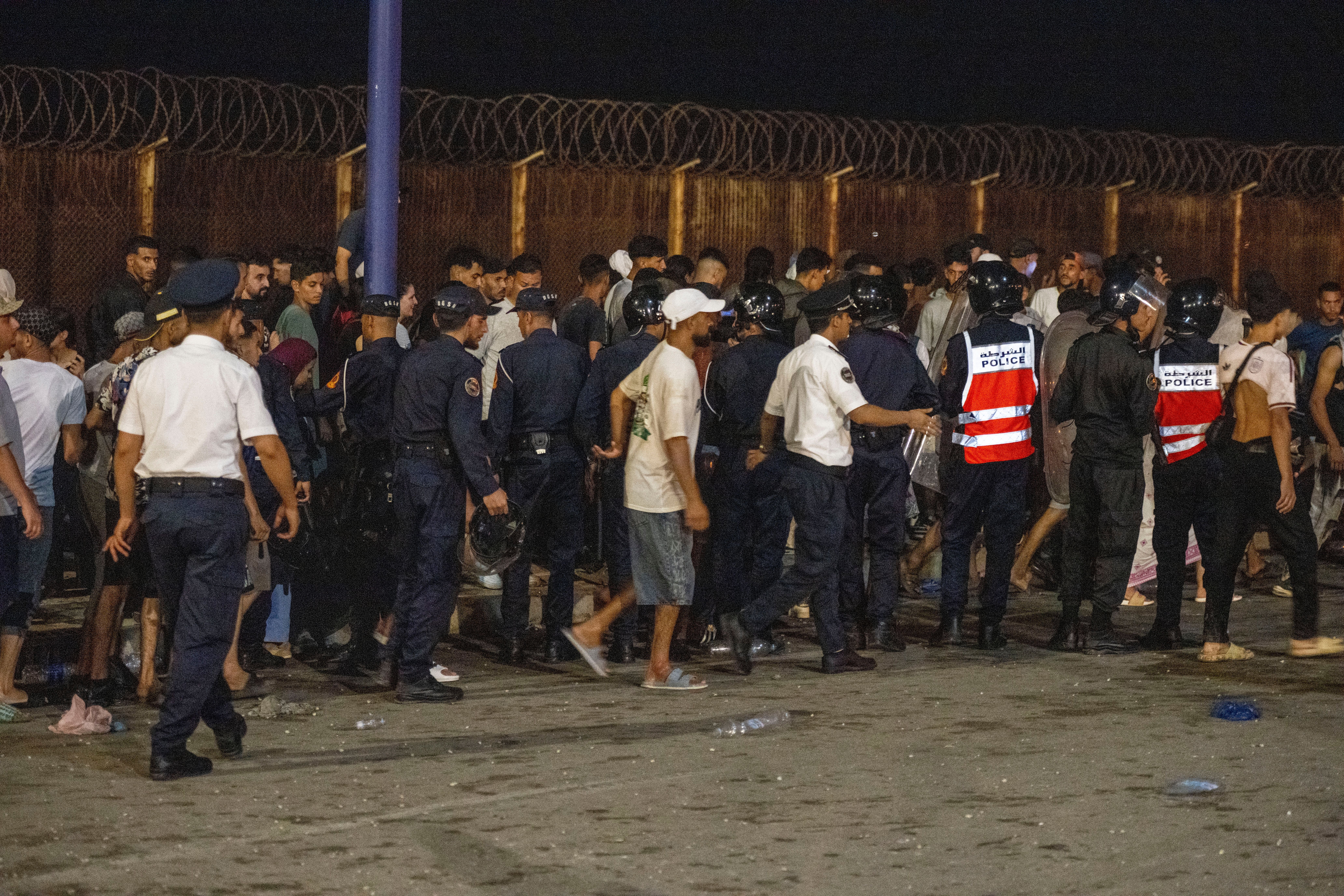Viele Menschen und Polizisten stehen nachts am Grenzzaun bei Bab Sebta zwischen Marokko und Ceuta.