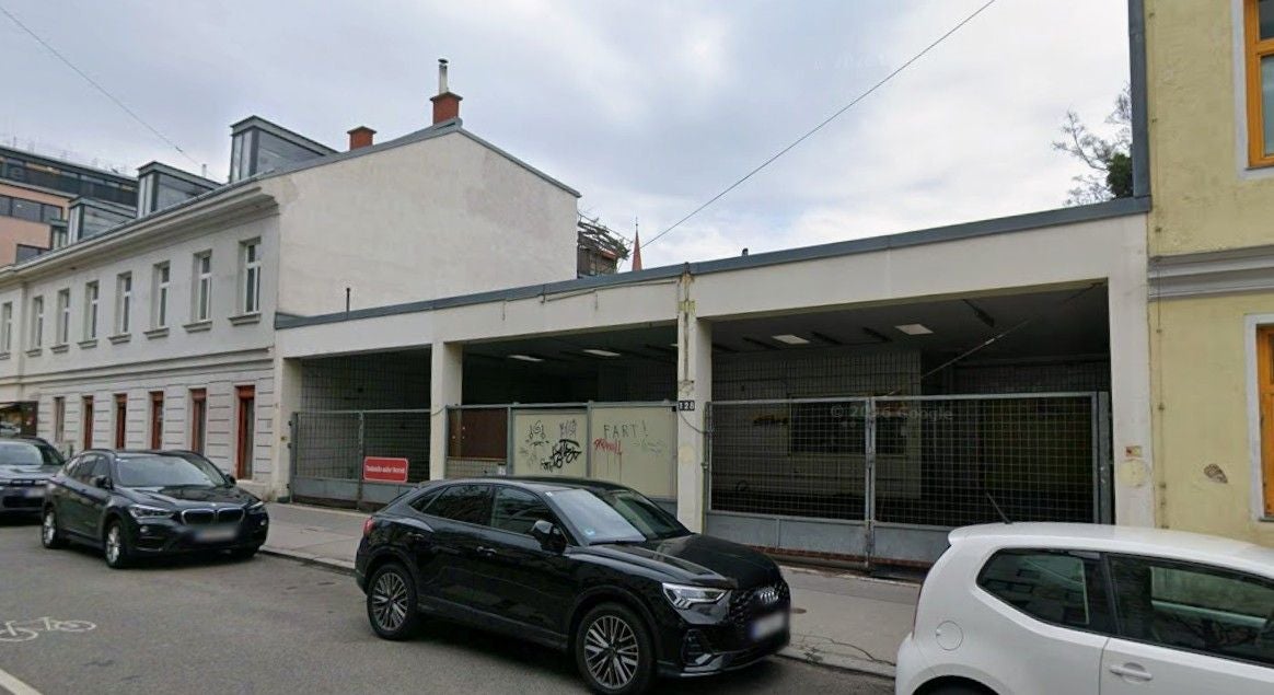 Gebäude mit umzäuntem Parkplatz in der Hasnerstraße 128 in Wien, Autos parken davor.